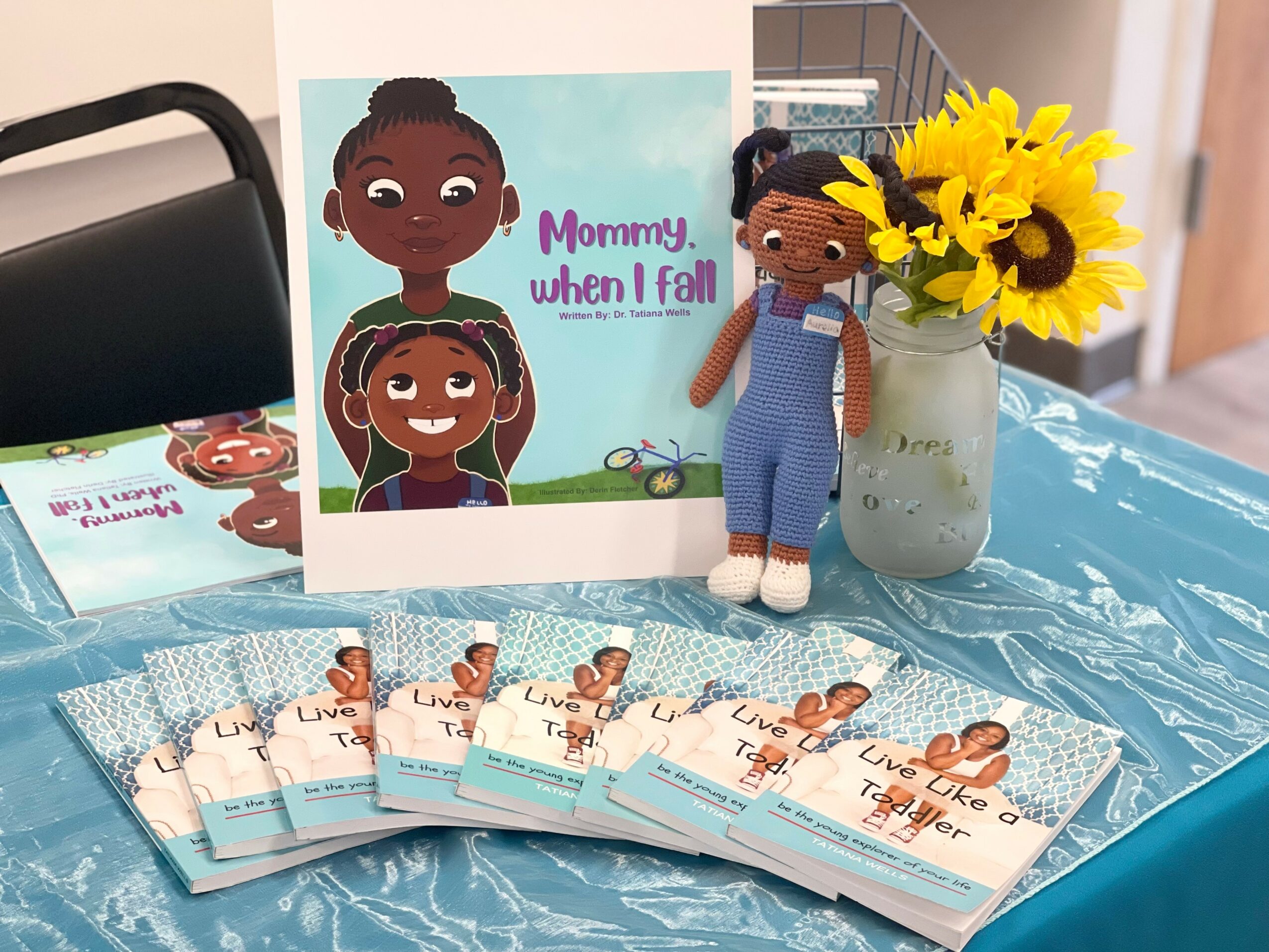 A card with two illustrated girls, a doll, sunflower bouquet, and several small cards on a blue tablecloth.