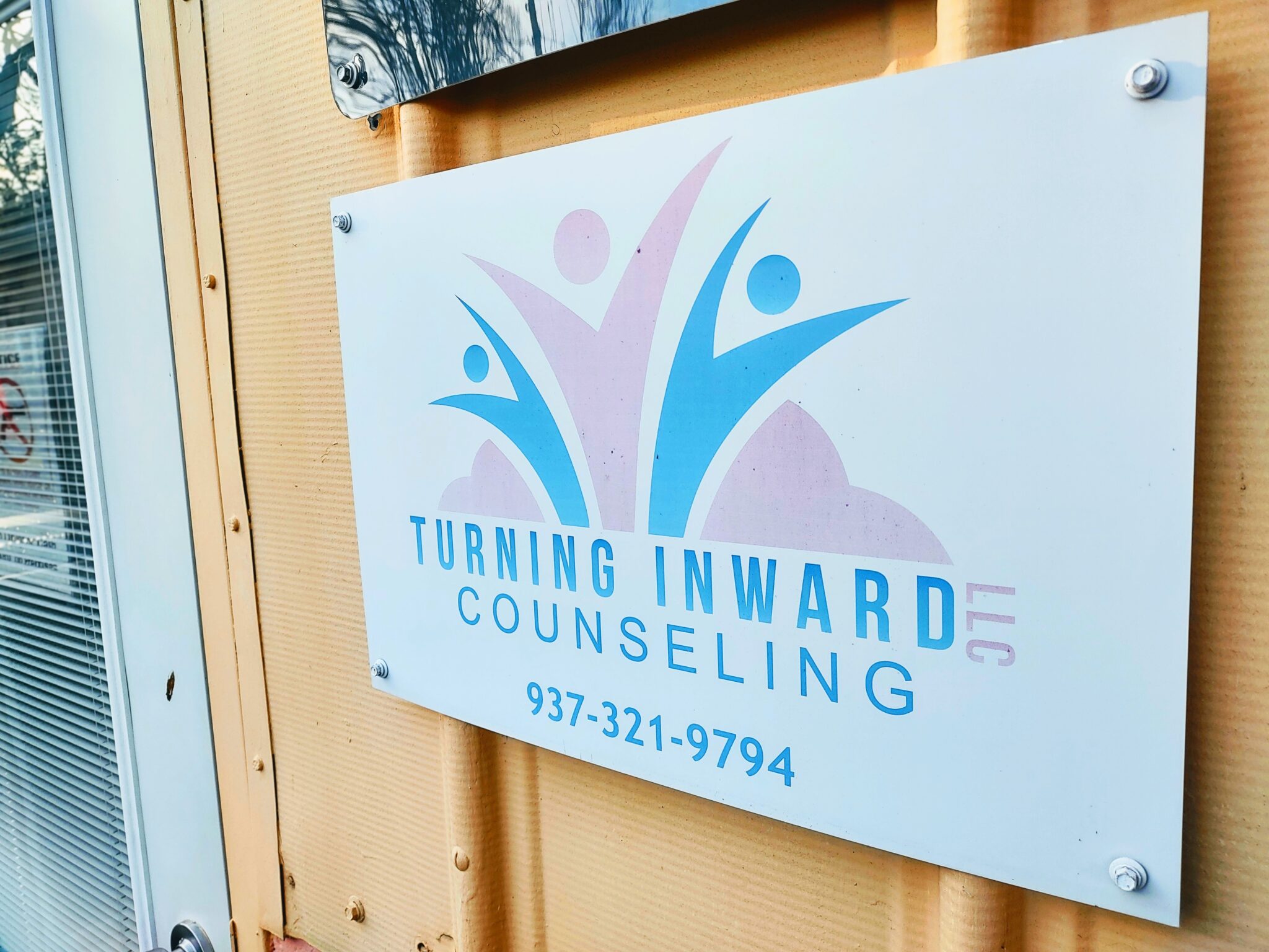 Sign for Turning Inward Counseling with logo, phone number, and company name on a wooden wall.