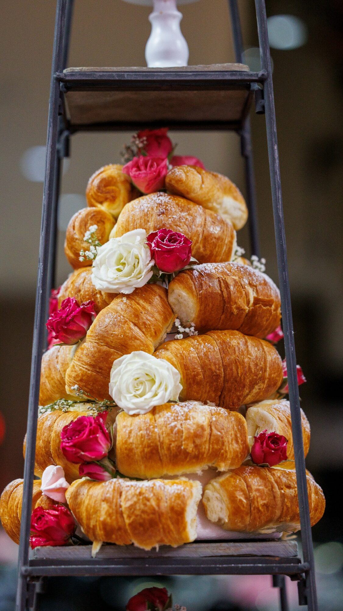 Stack of croissants decorated with white and pink roses on a black metal stand.