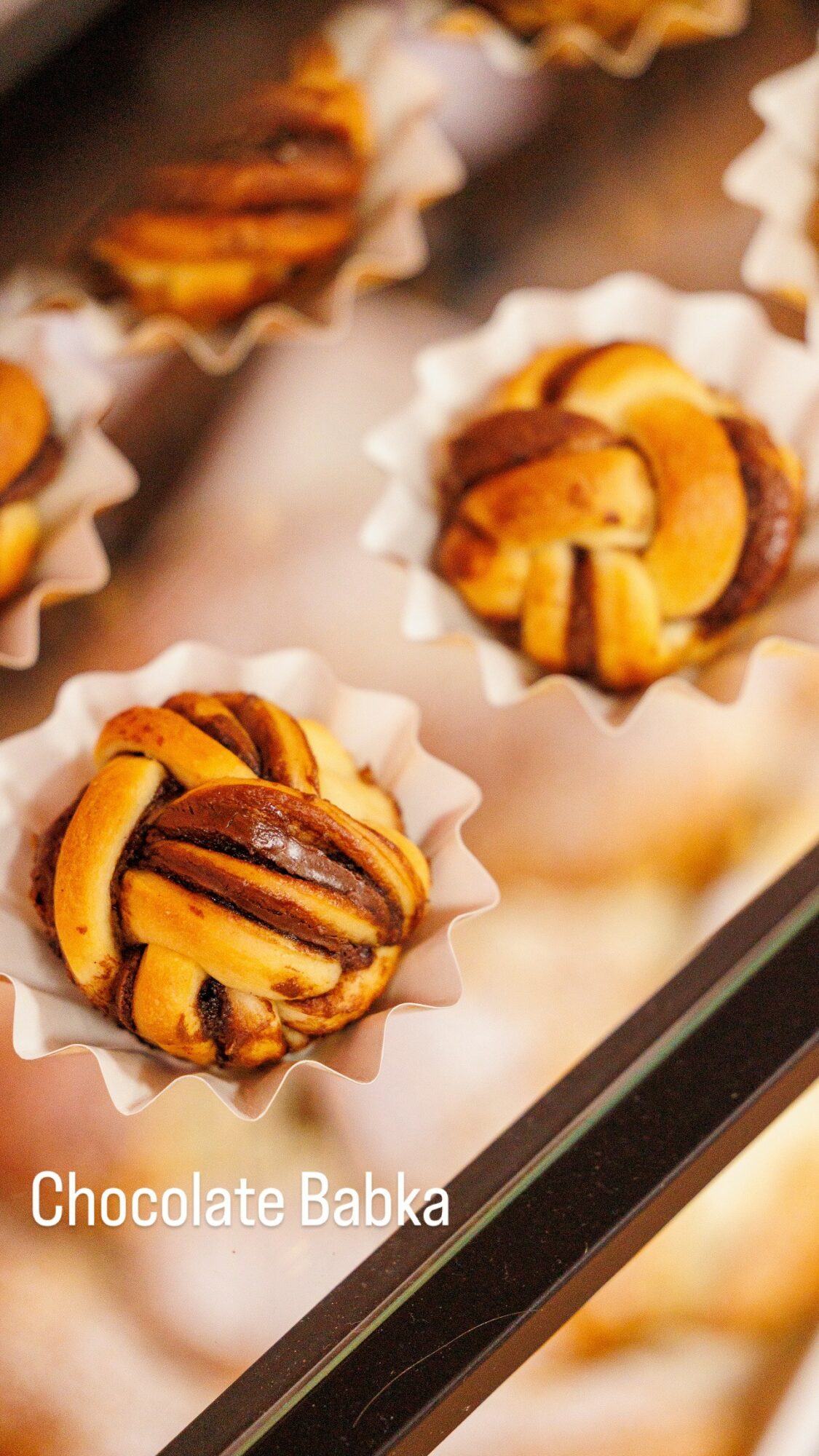 Assorted chocolate babka pastries in paper cups on a tray, with swirls of chocolate and yellow dough visible.