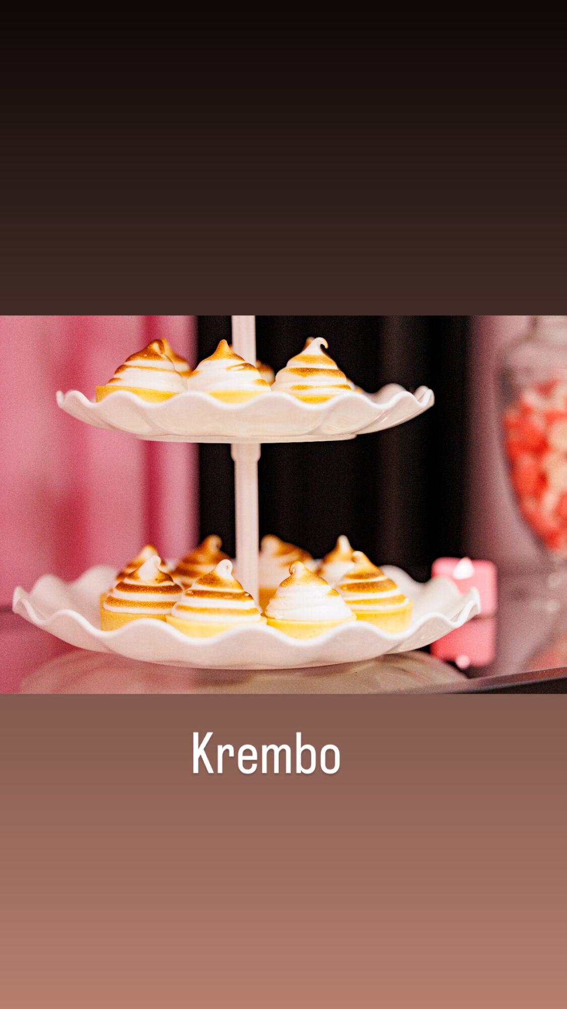 Two-tiered dessert stand with cream and caramel desserts, pink background, and blurred objects, labeled 'Krembo'.