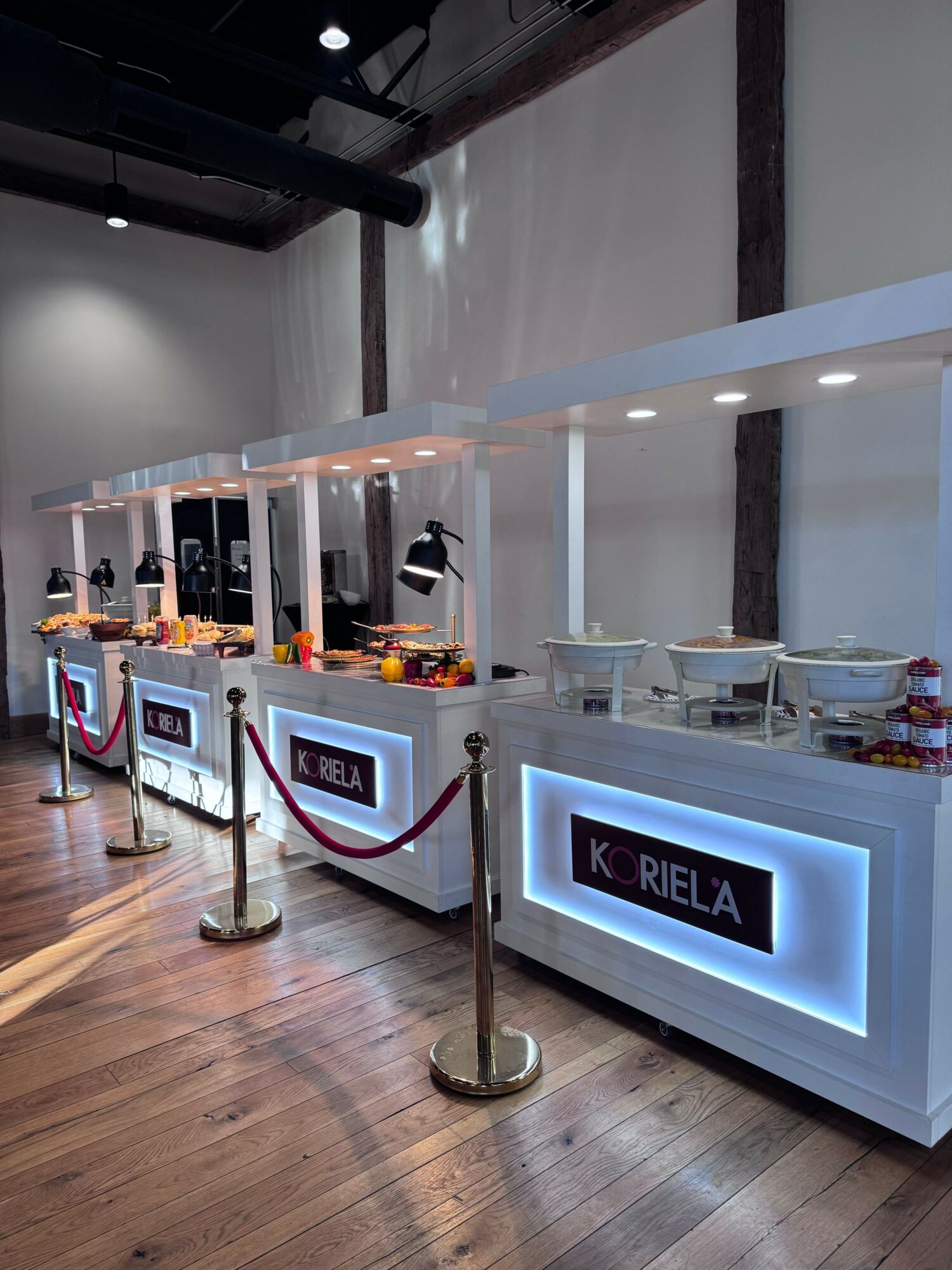 Display counter with illuminated sign, snacks, and drinks on a wooden floor, viewed from the side.