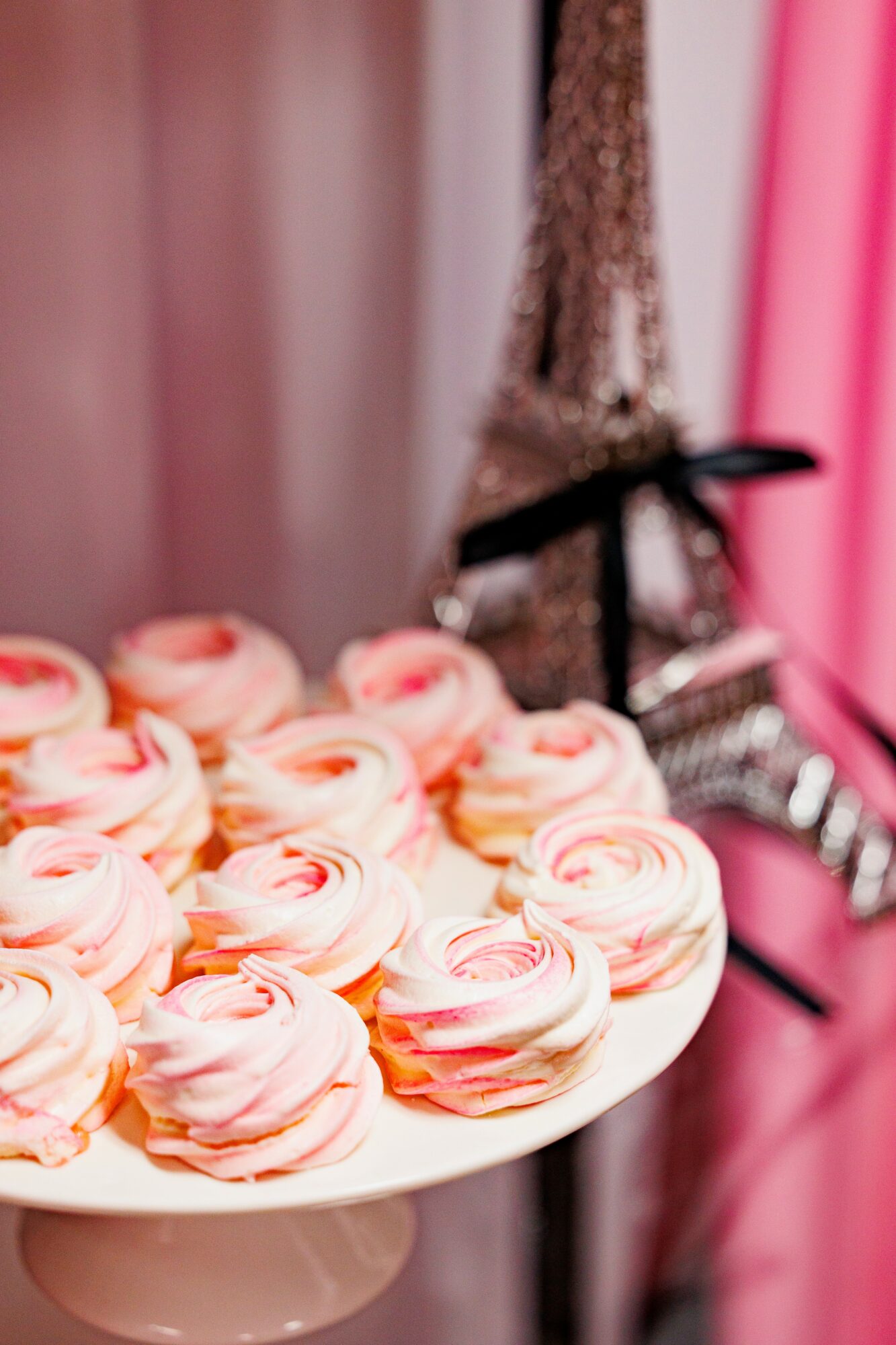 Pink and white swirled cupcakes on a white cake stand with a blurred Eiffel Tower decoration in the background.