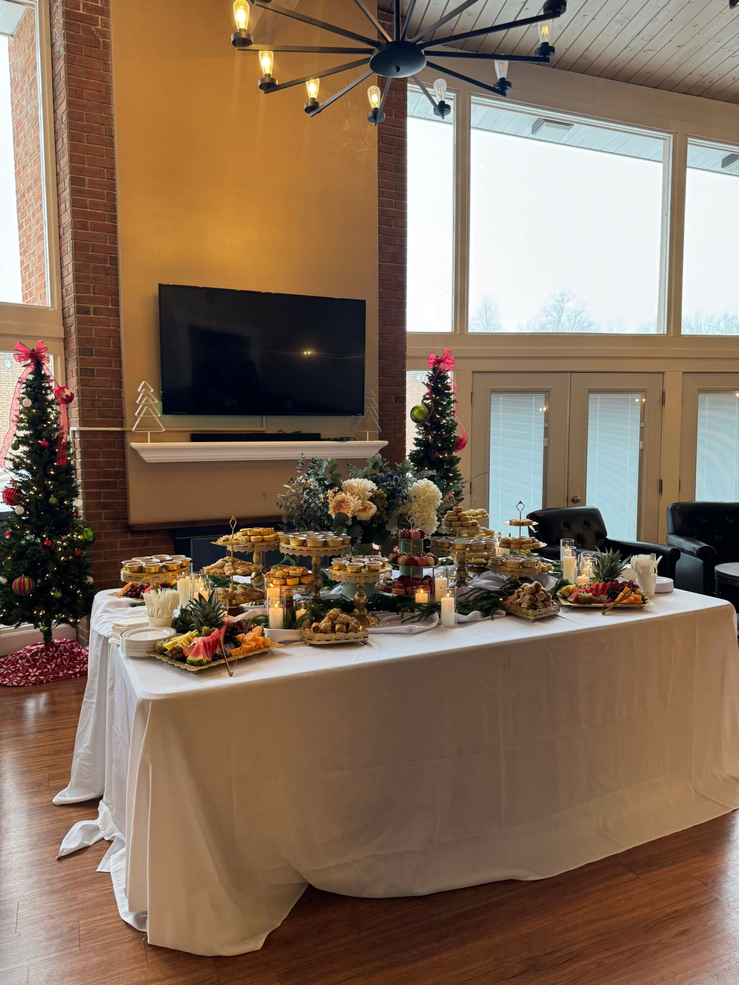 Table with food and decorations, TV on wall, window with view, Christmas trees, and chandelier, all viewed sideways.