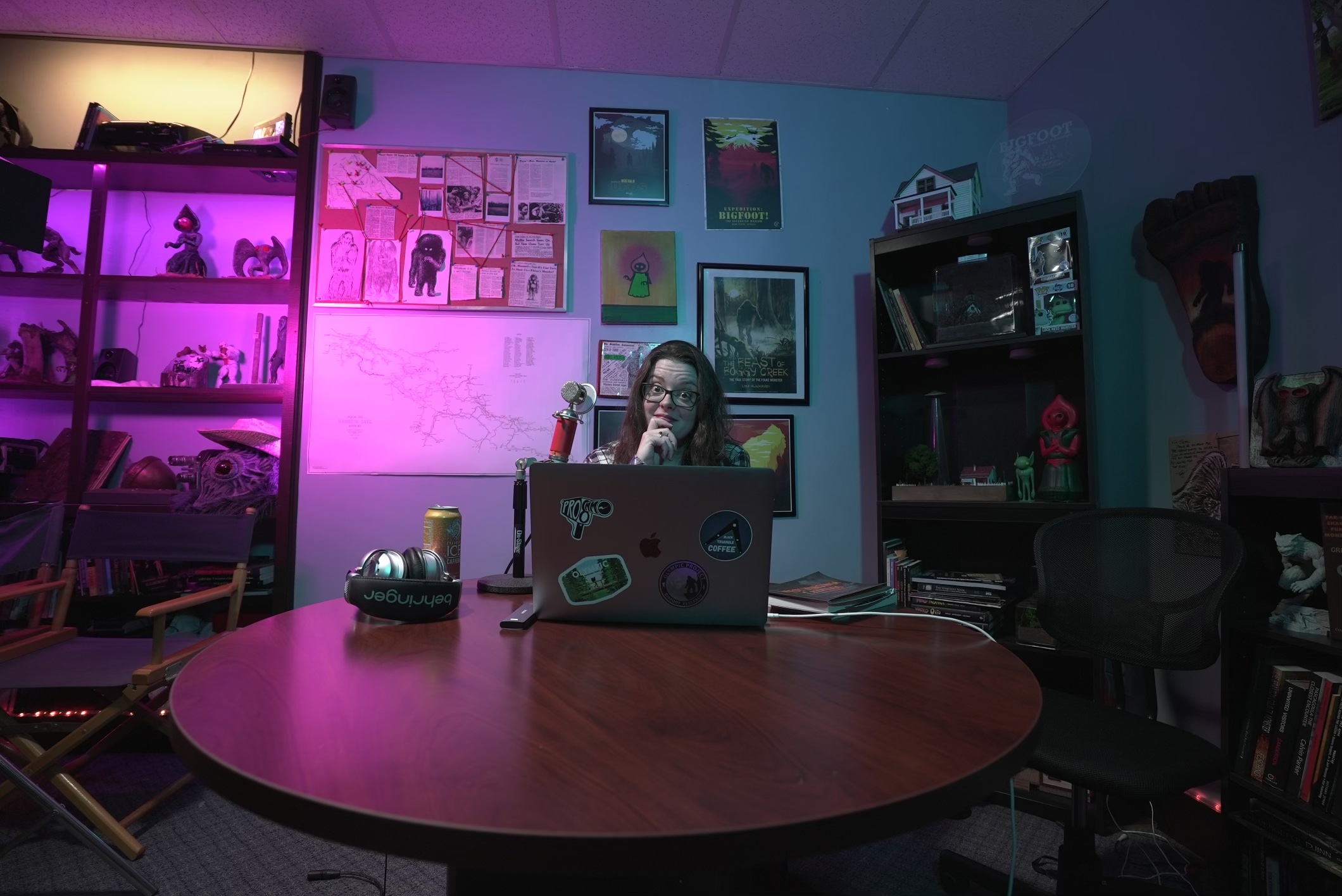 Person sitting at a desk in a room with colorful wall art and shelves, illuminated by pink and blue lighting.