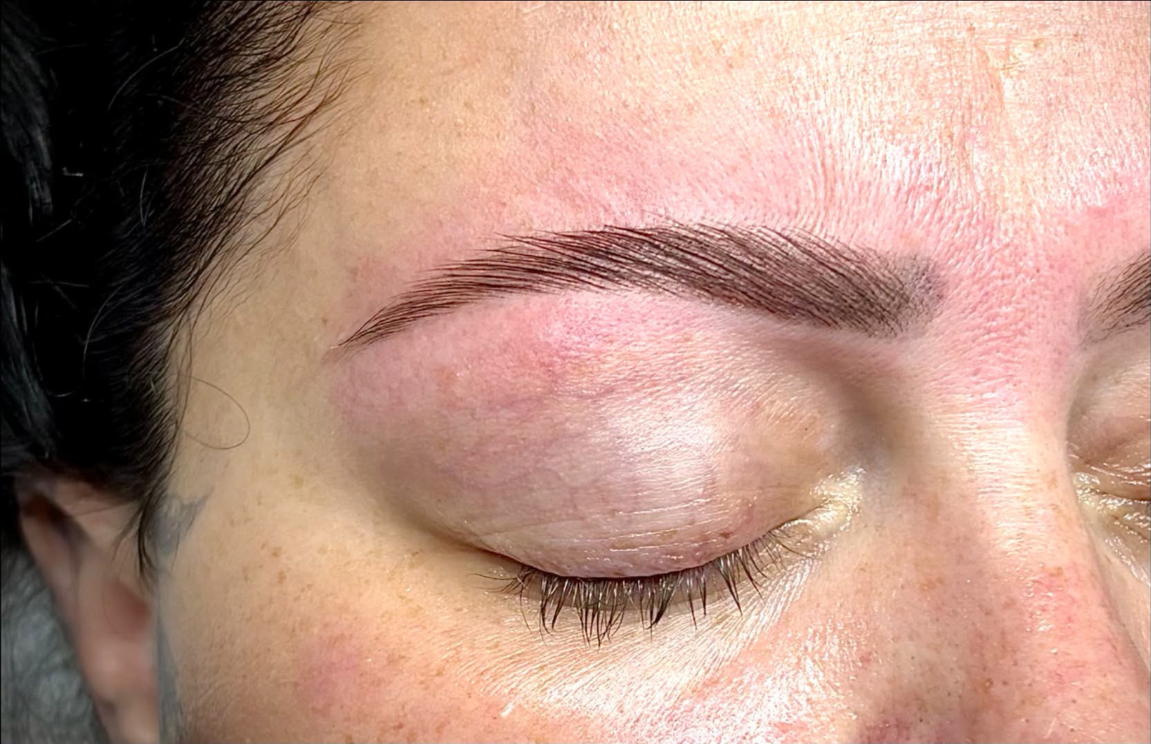 Close-up of a person's face with closed eyes, showing well-groomed eyebrows and smooth skin.