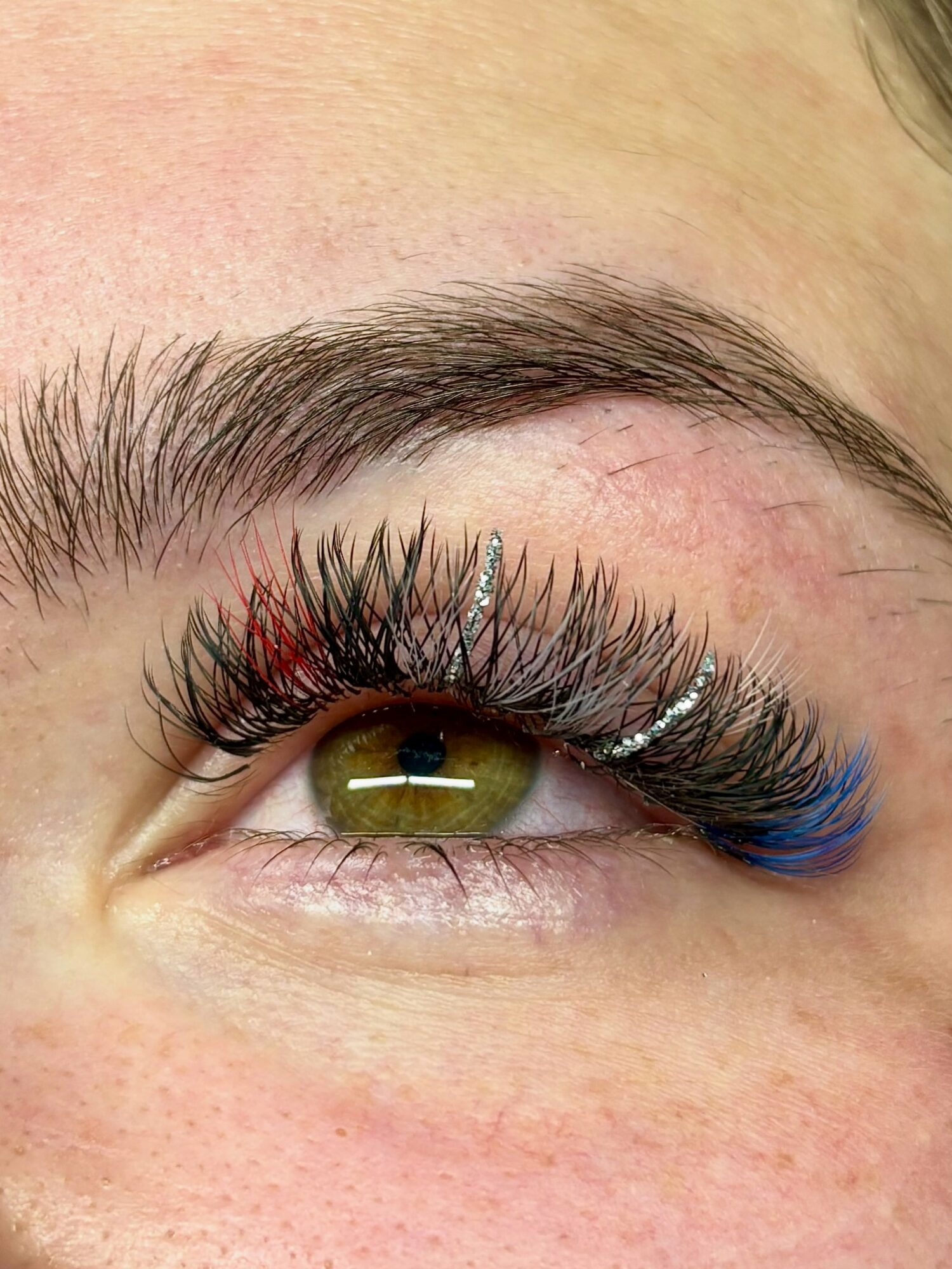 Close-up of a person's eye with makeup, including long eyelashes and blue eyeliner, and visible eyebrow hairs.