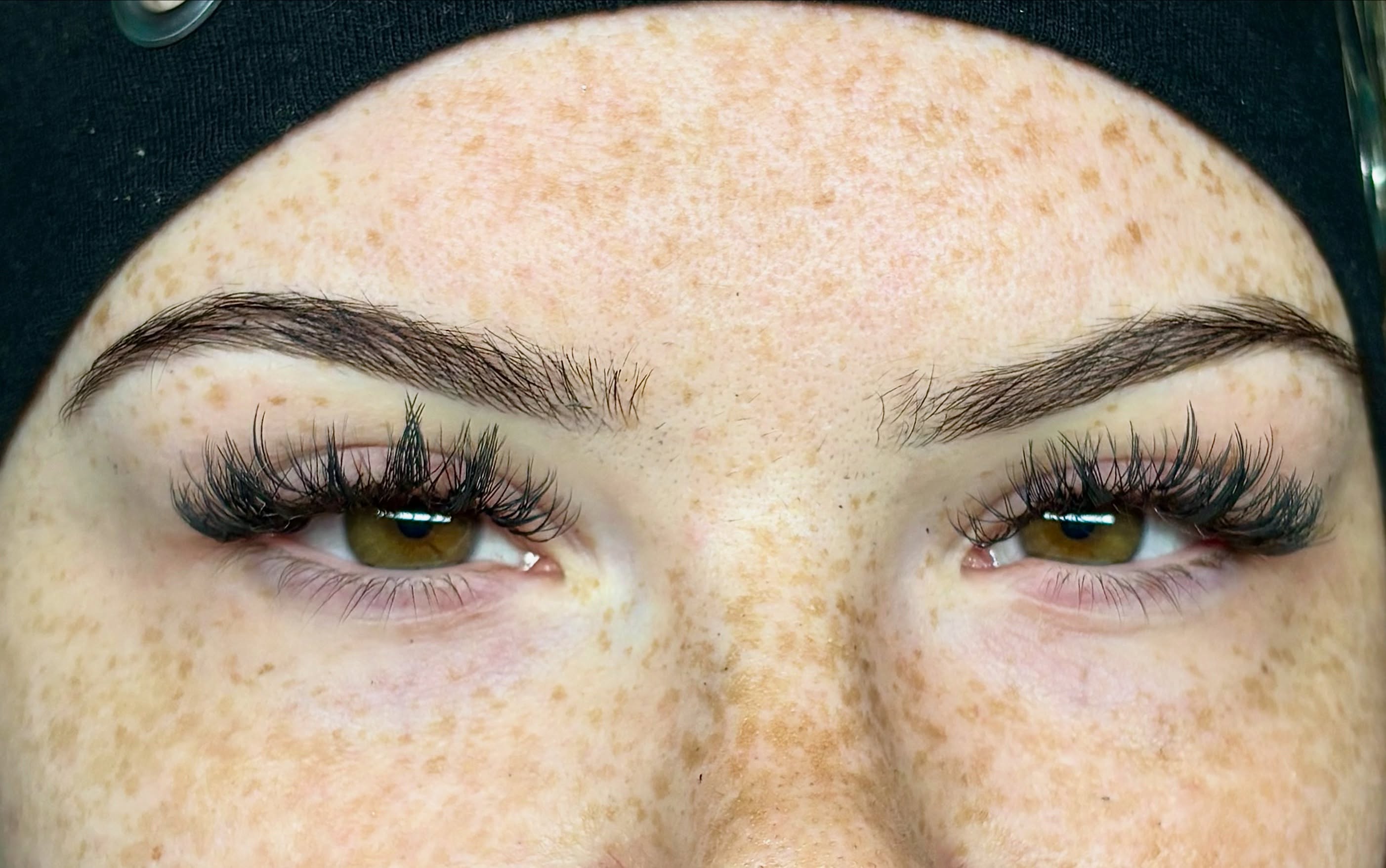 Close-up of a person's eyes with well-groomed eyebrows and long eyelashes, showing freckles on the skin.