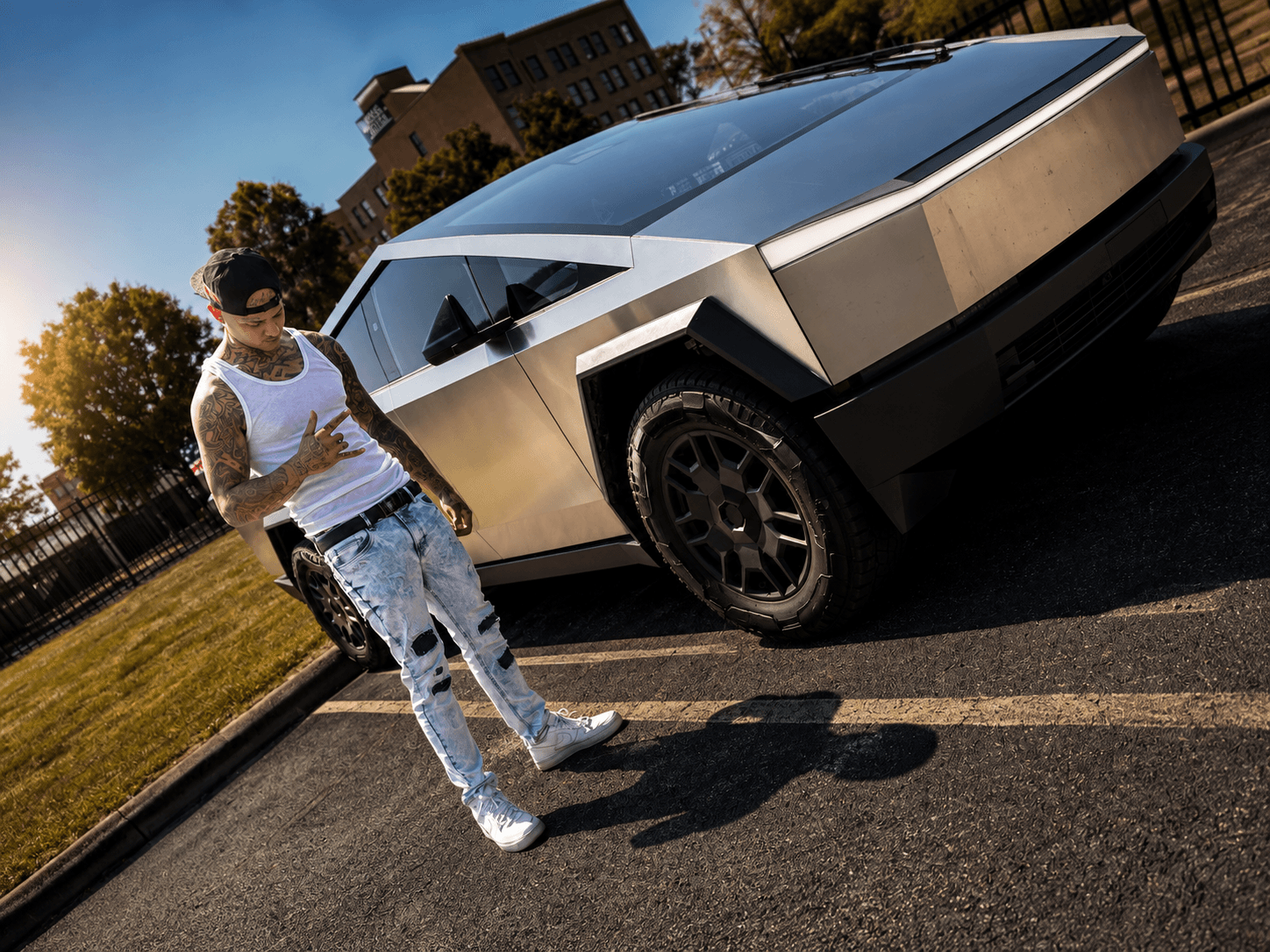 Person standing next to a futuristic silver car on a street, with trees and buildings in the background.