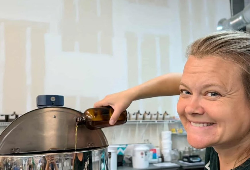 Woman smiling while using a knife to cut a large pot lid in a kitchen.
