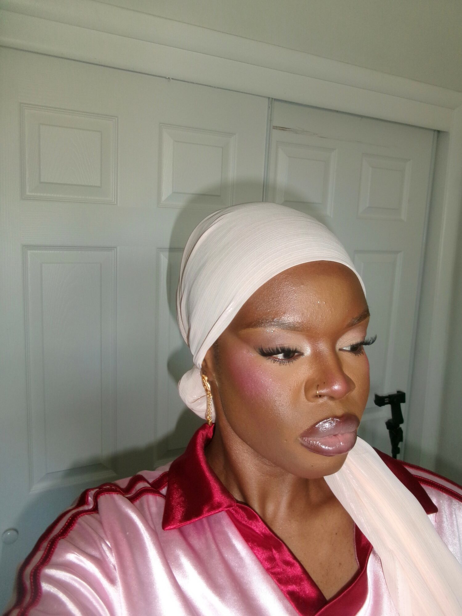 Woman wearing a white headscarf and red satin shirt, looking to the side, with a neutral background.