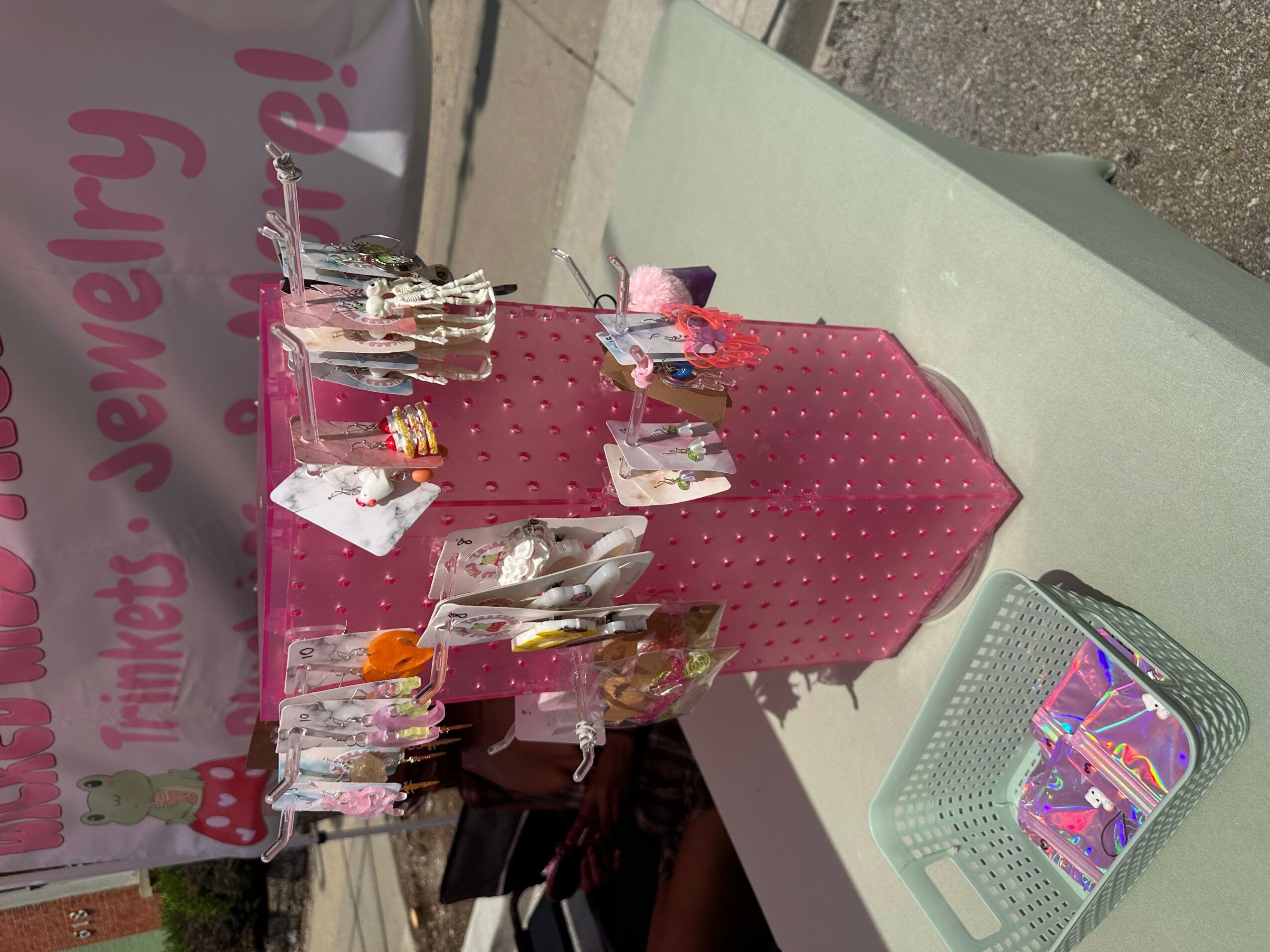 Display of jewelry on a pink stand with a pink polka dot cover, on a white table outdoors.