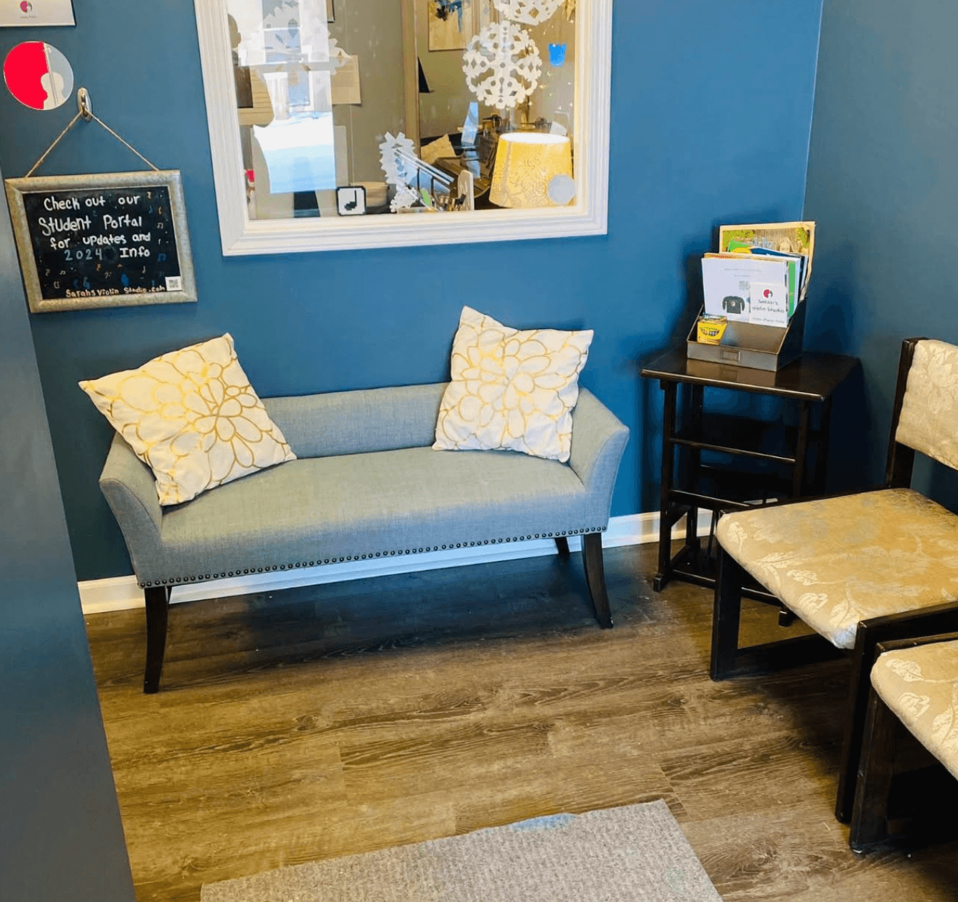 Small seating area with a light blue sofa, two yellow pillows, a black side table with magazines, and a beige chair.