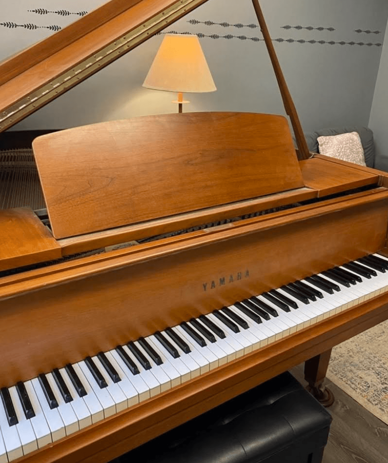 Upright wooden Yamaha grand piano with open lid, a lamp, and a room with a rug in the background.