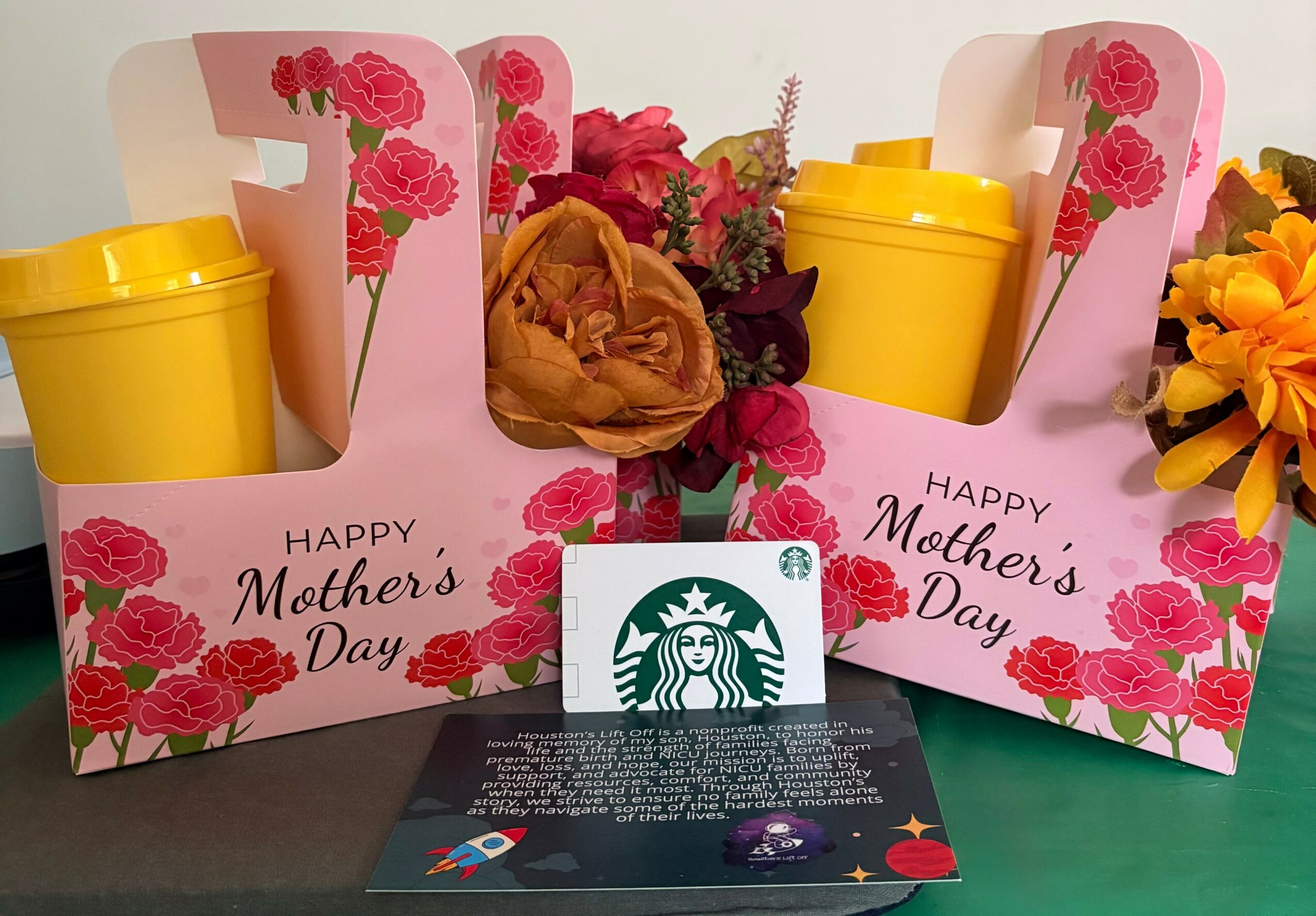 Two Mother's Day gift boxes with yellow cups, flowers, and a Starbucks card, on a green surface.