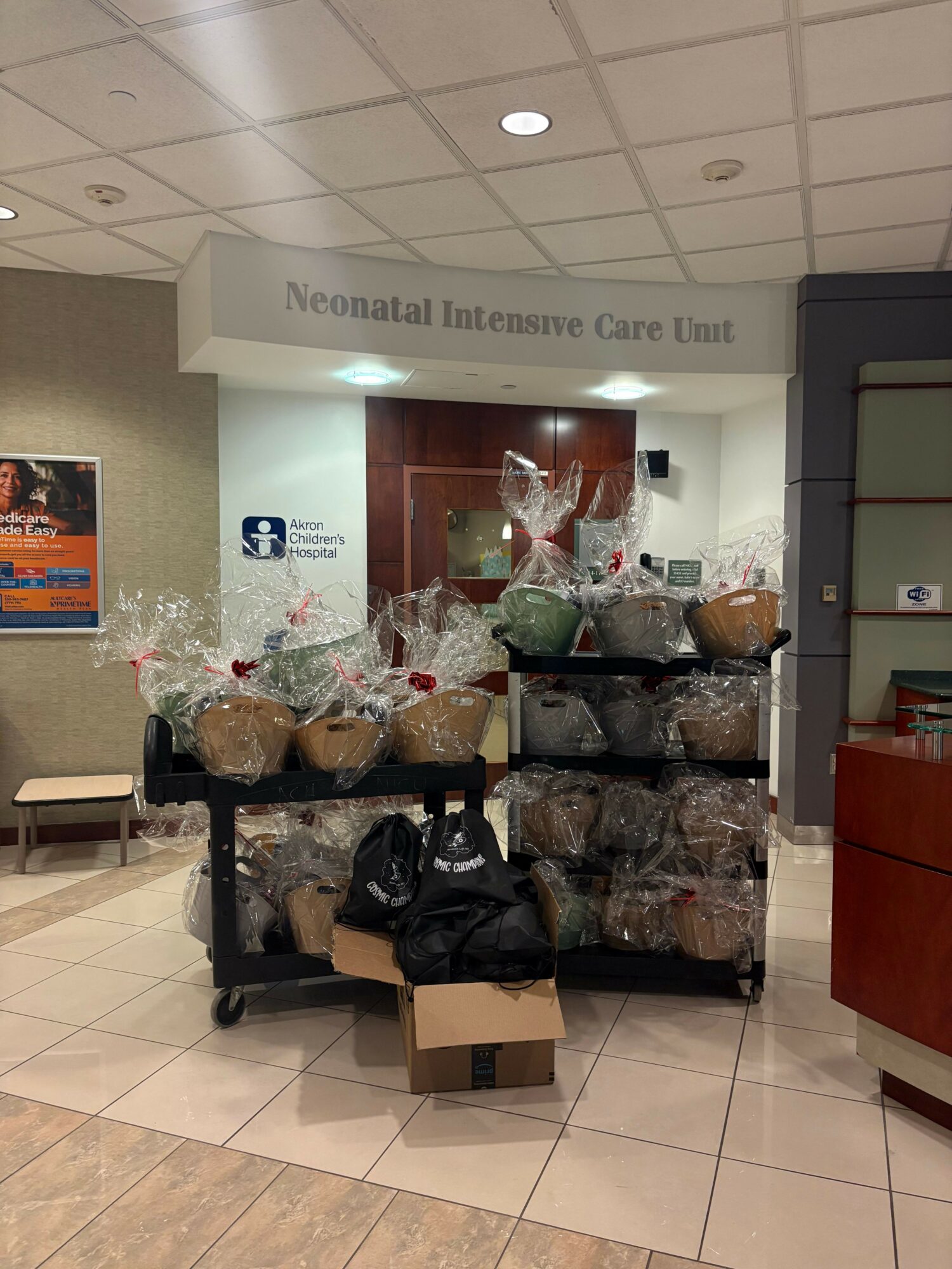 Display of holiday decorations with wrapped gifts, flowers, and a sign in a lobby area.