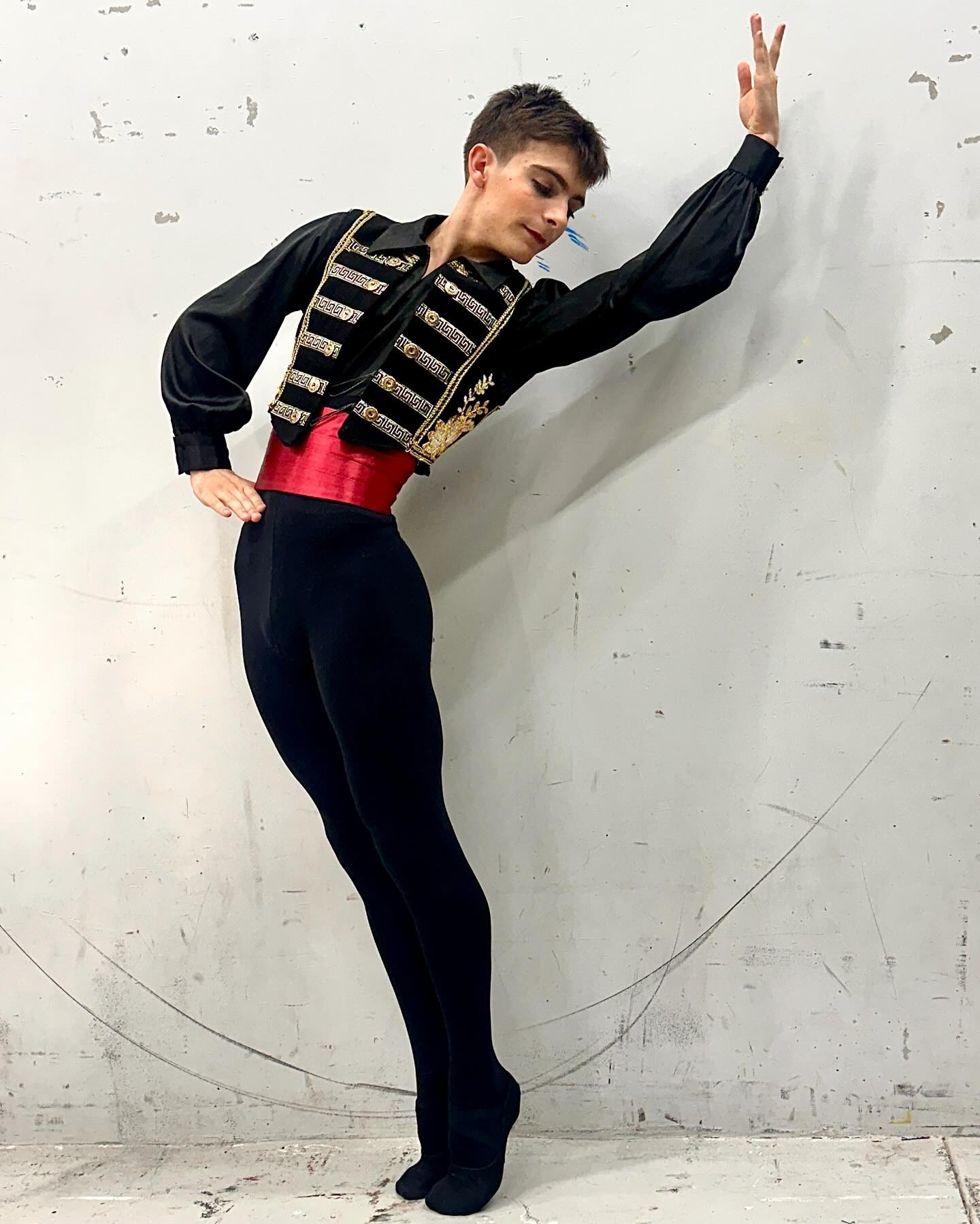 Person in a costume poses with one arm raised and the other on their hip against a plain wall.