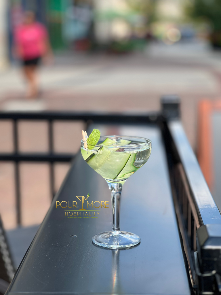 A cocktail glass with a lime wedge on a black table outdoors, blurred background of a street scene.