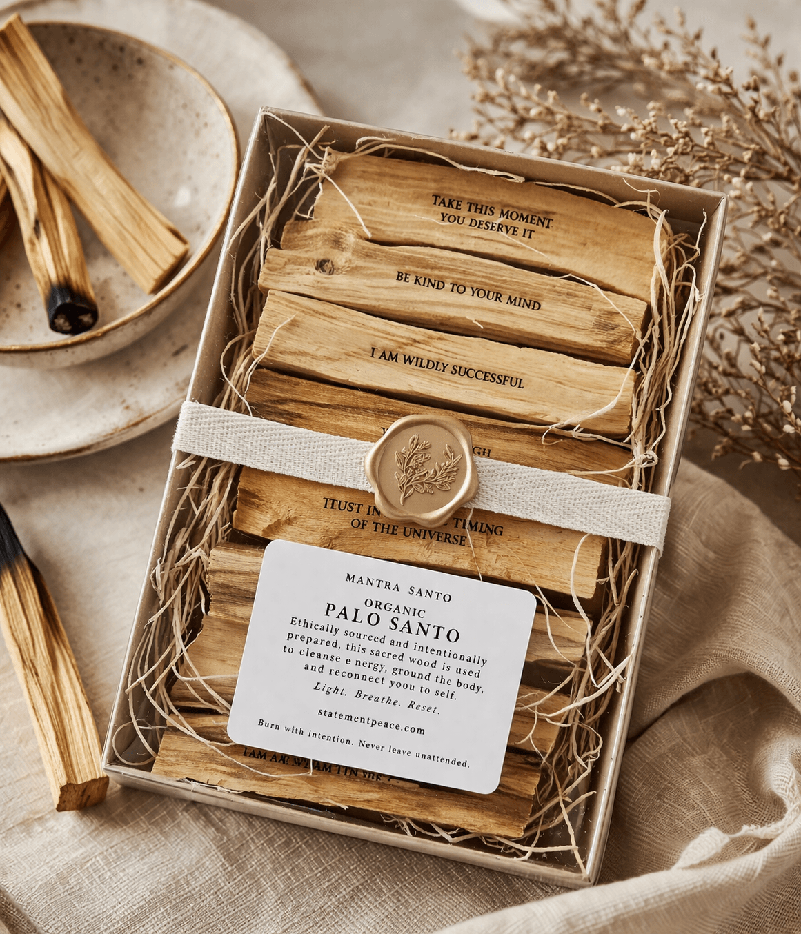 Box of wooden cards with inspirational messages, a wax seal, and a card about organic palo santo, on a beige fabric surface.