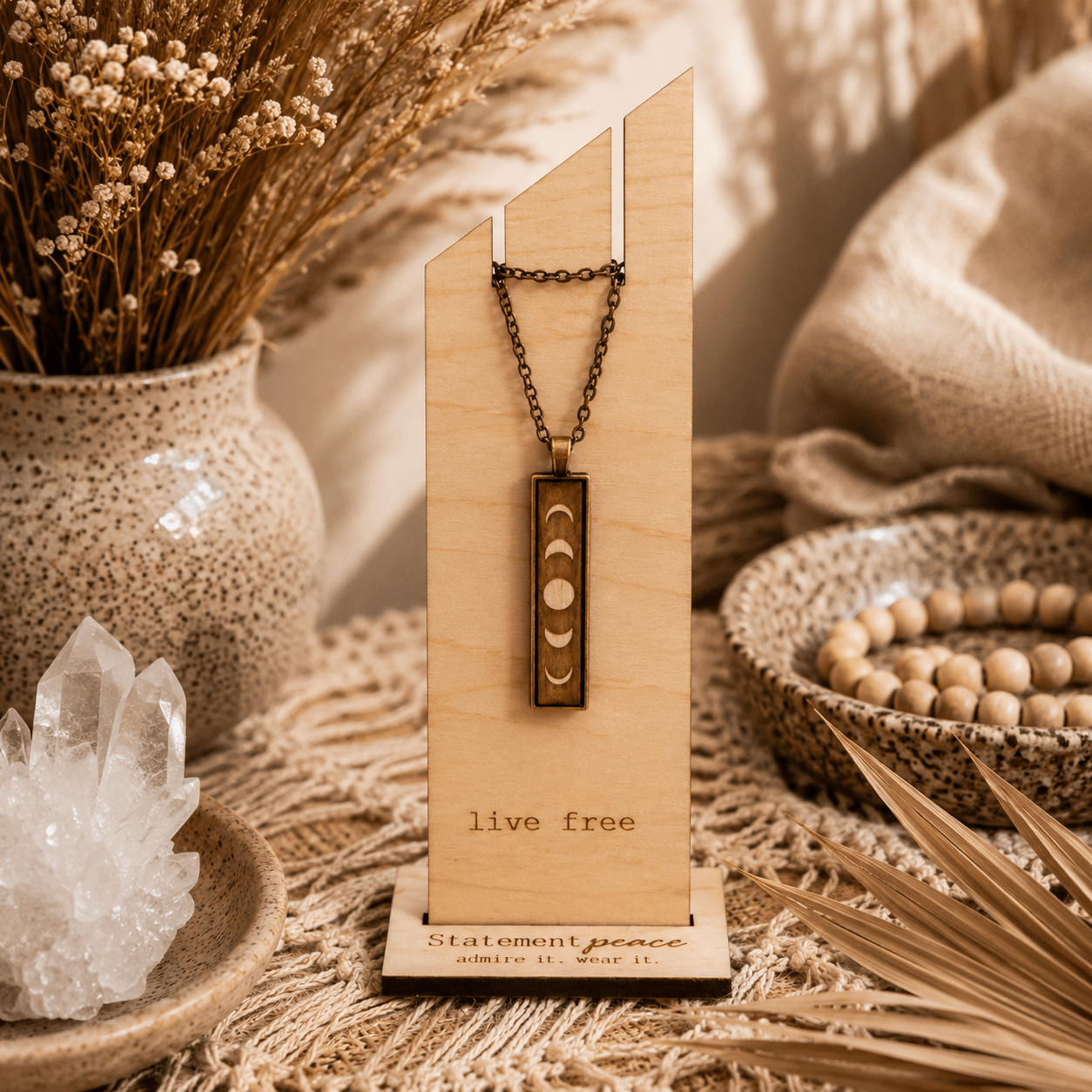 Pendant necklace with geometric design on a wooden display, surrounded by decorative items and dried plants, with a warm, cozy background.