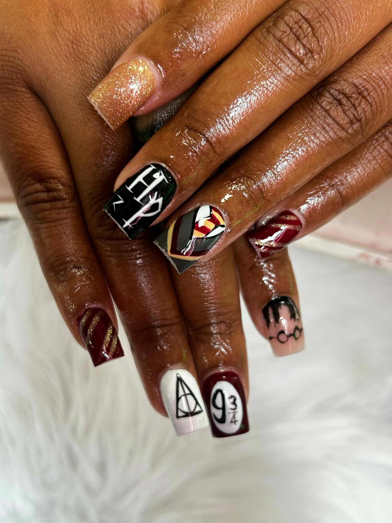 Close-up of hands with decorated nails, featuring various designs and colors, resting on a white furry surface.