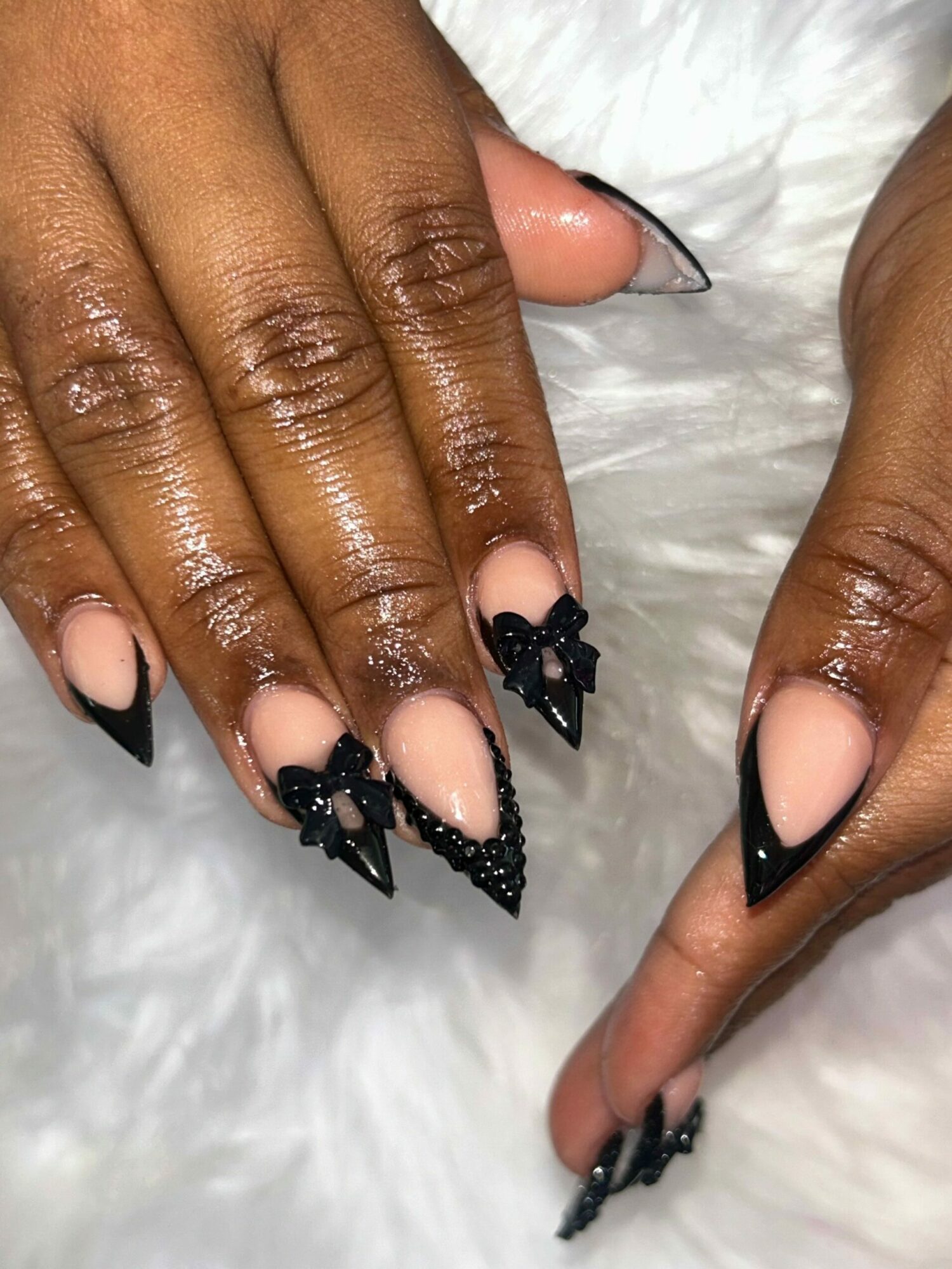 Close-up of hands with long, black, pointed, decorated nails resting on a white furry surface.