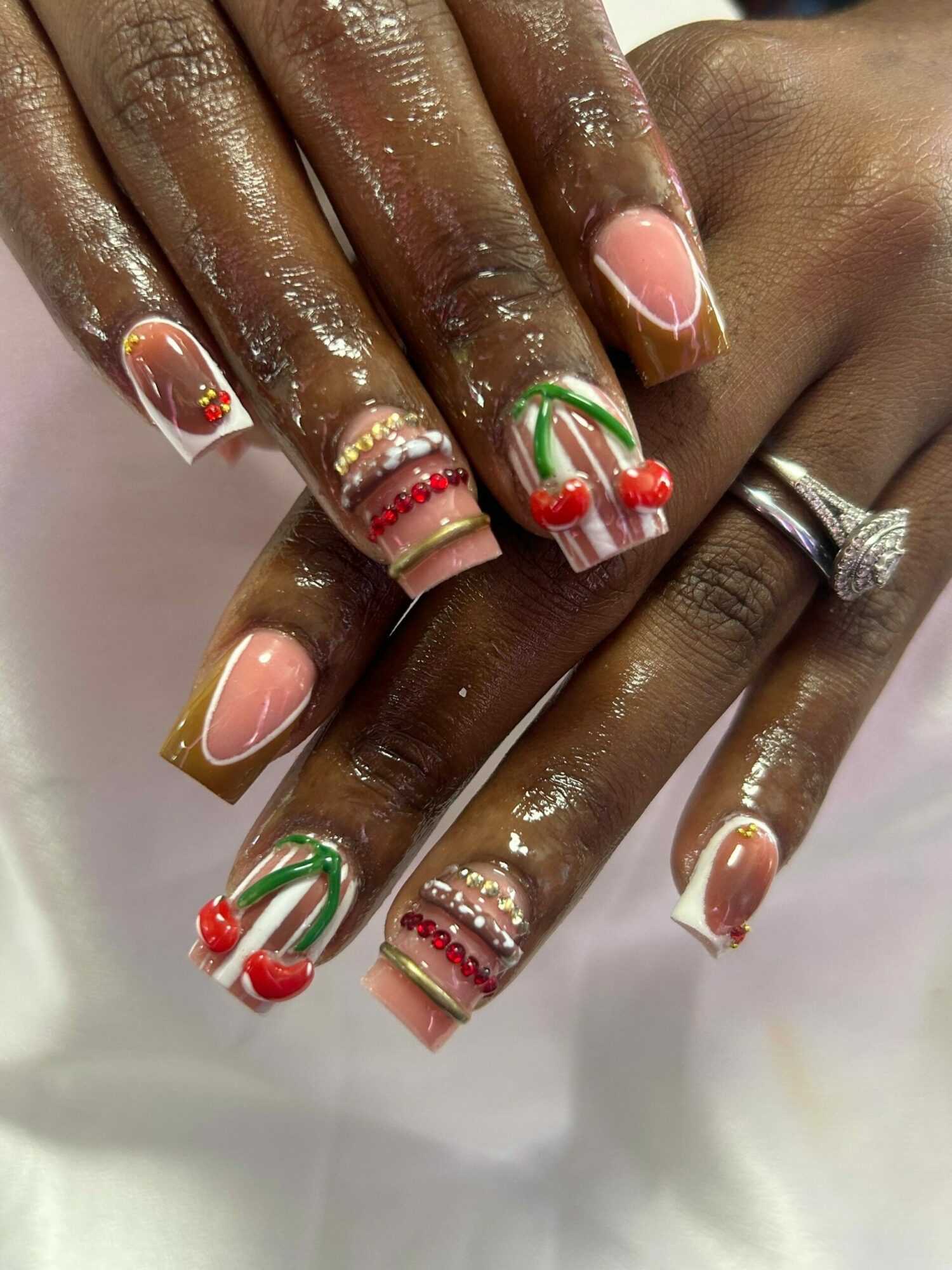 Close-up of hands with decorated nails, some with red, green, and white designs, and a ring on one finger.