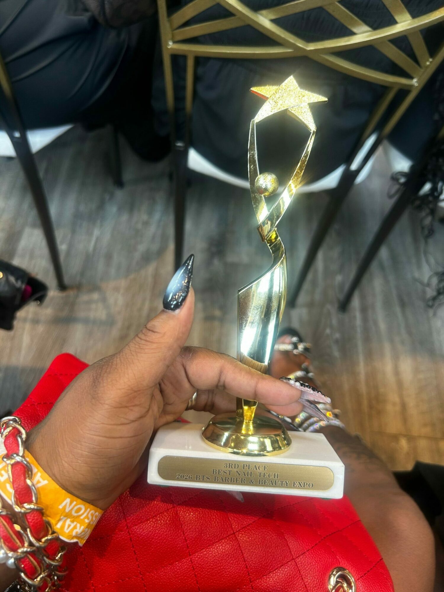 Person holding a star-shaped trophy with a gold base, sitting on a red quilted surface, with a wristband and jewelry visible.