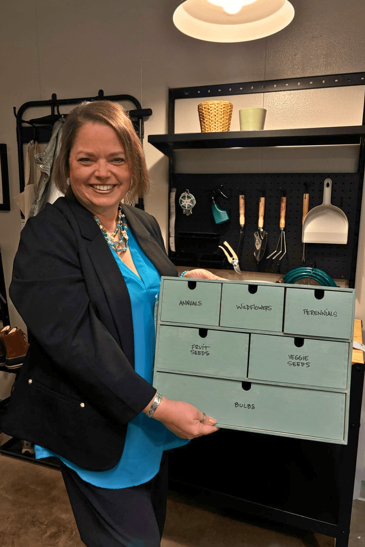 Woman smiling, holding a whiteboard with labeled sections, standing in a room with kitchen utensils and shelves.