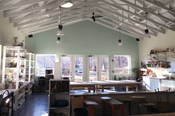 Interior of a bright room with high white ceiling, large windows, shelves, tables, and chairs, sunlight streaming in.