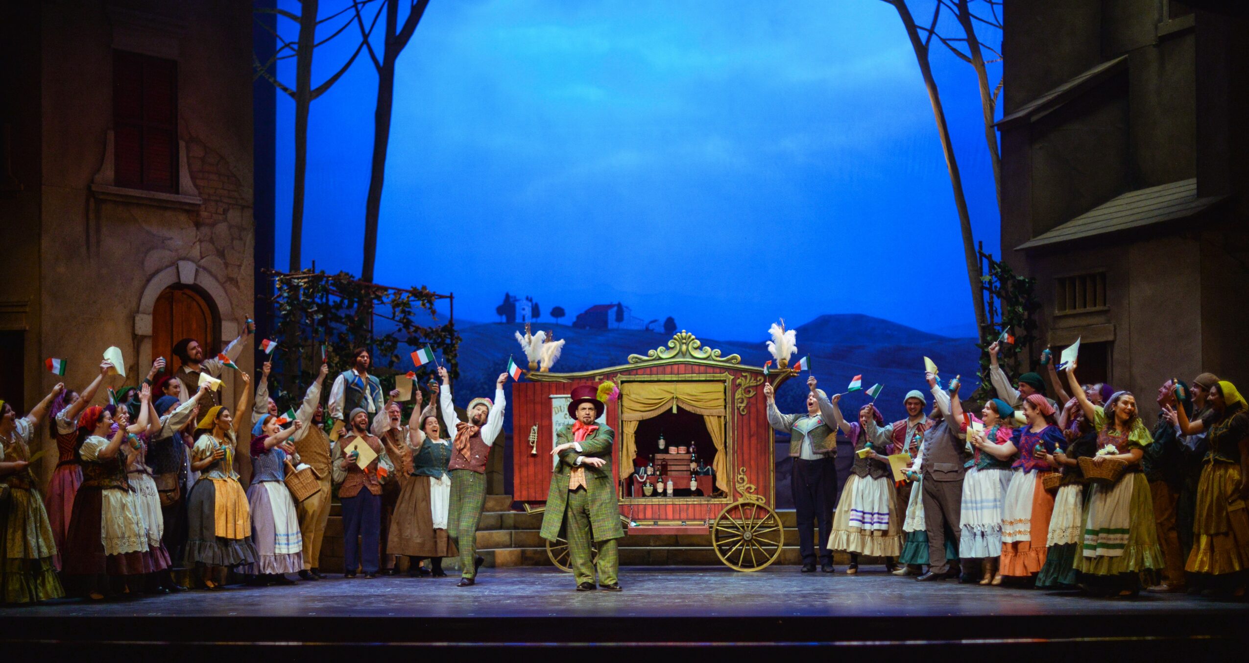 Theater stage with actors in period costumes, a carriage, and a backdrop of a blue sky and landscape.