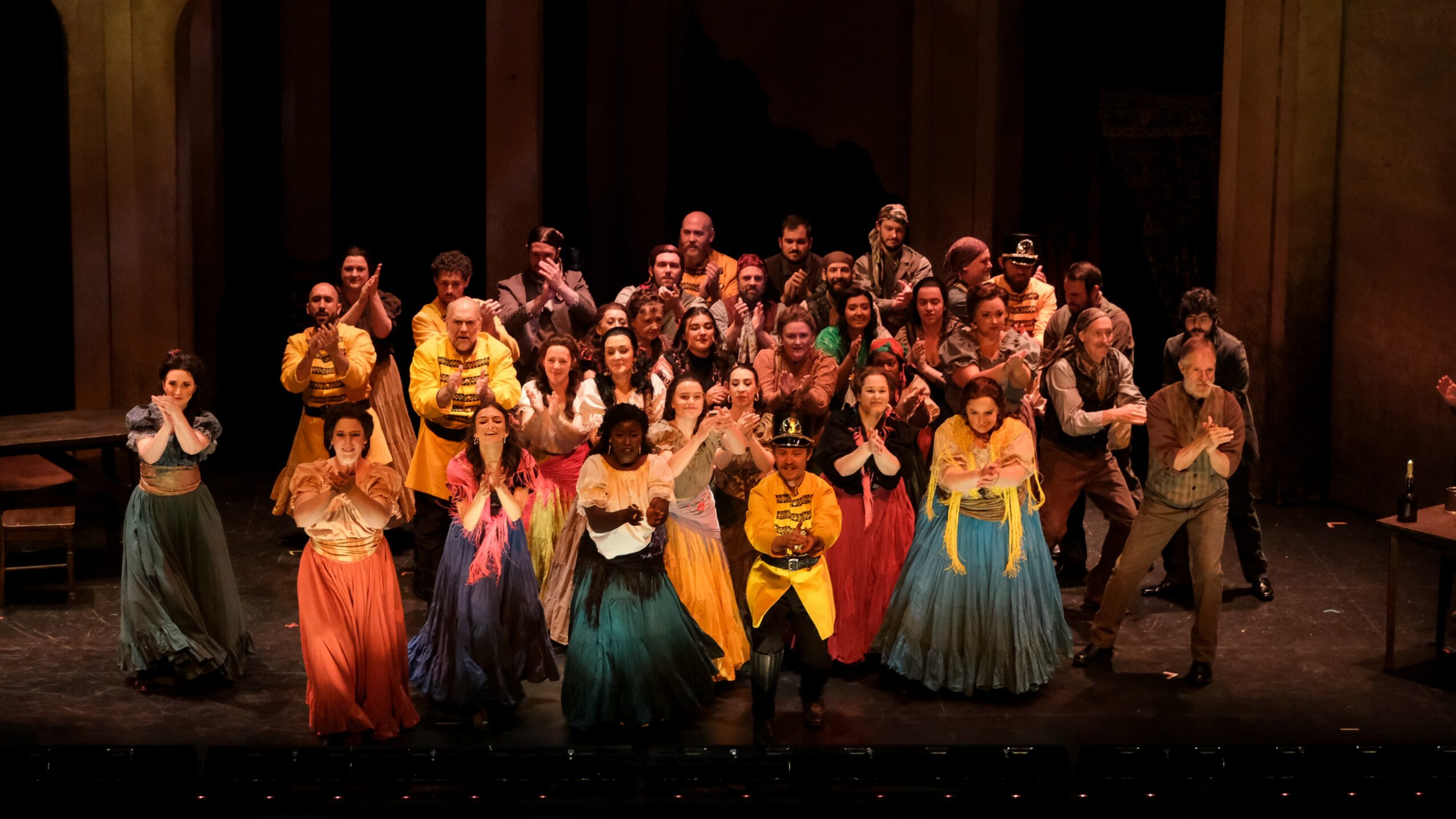 Group of performers on stage in colorful costumes, posing for a photo after a performance.