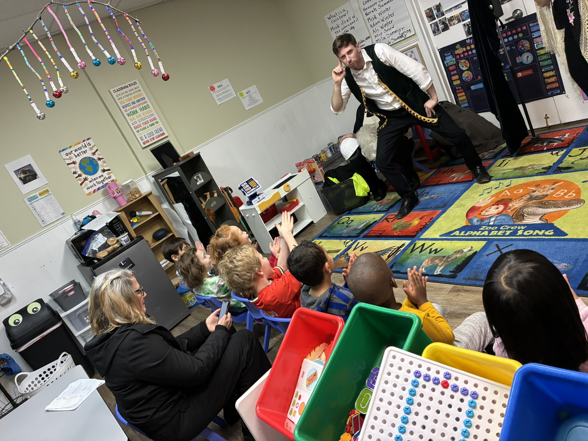 A performer with a saxophone entertains children seated on a colorful carpet in a classroom.