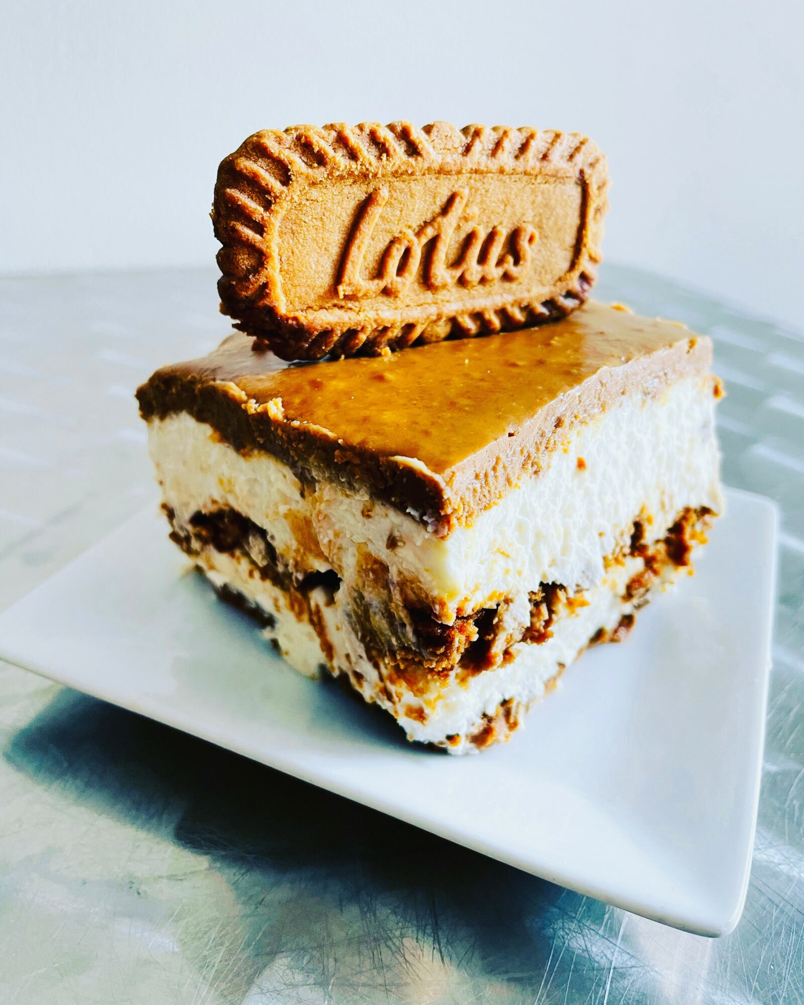 A layered dessert with a biscuit on top, placed on a white plate, with a light background.