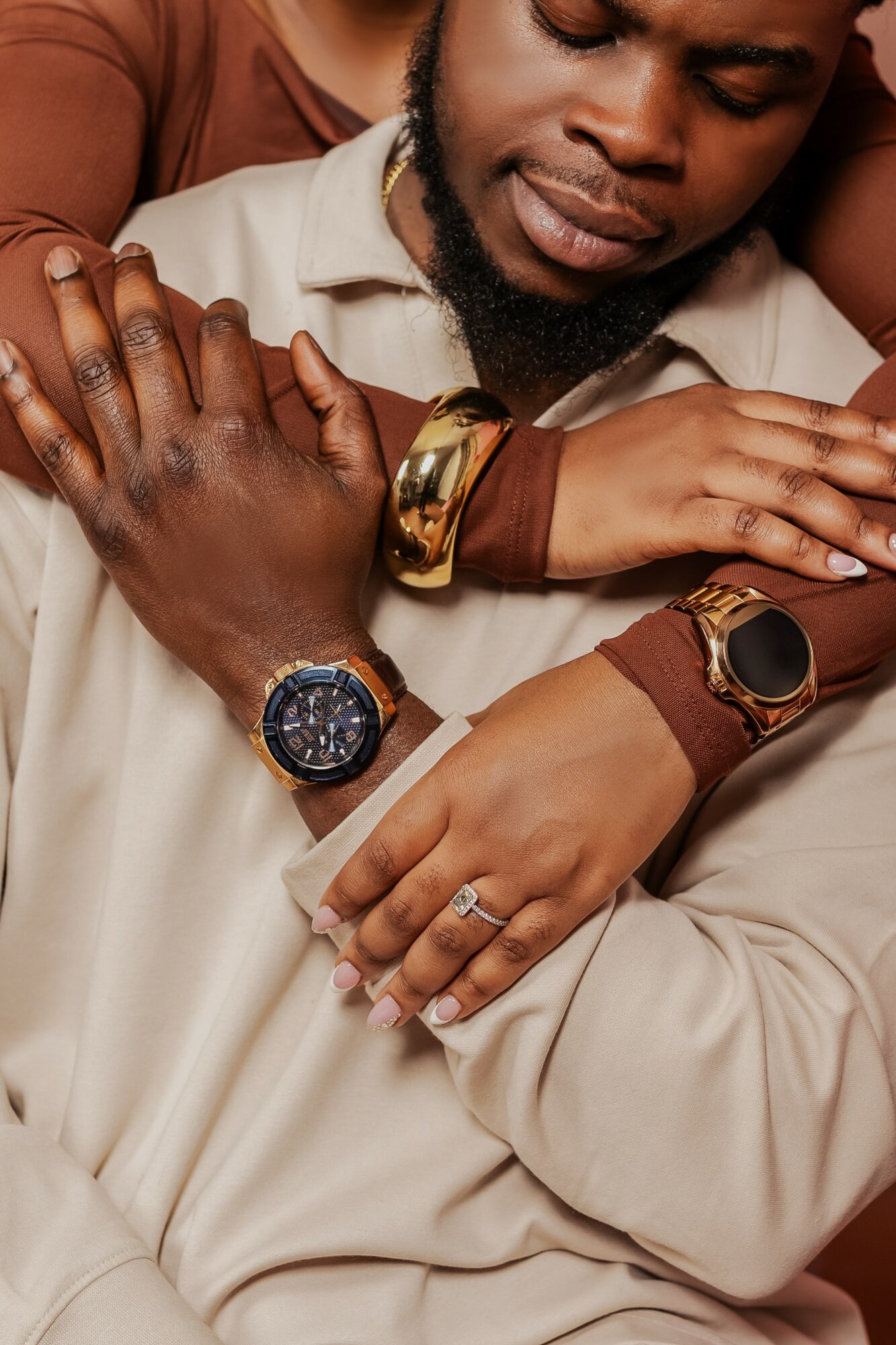Close-up of a man with multiple watches and rings, with a woman embracing him, showing affection and closeness.