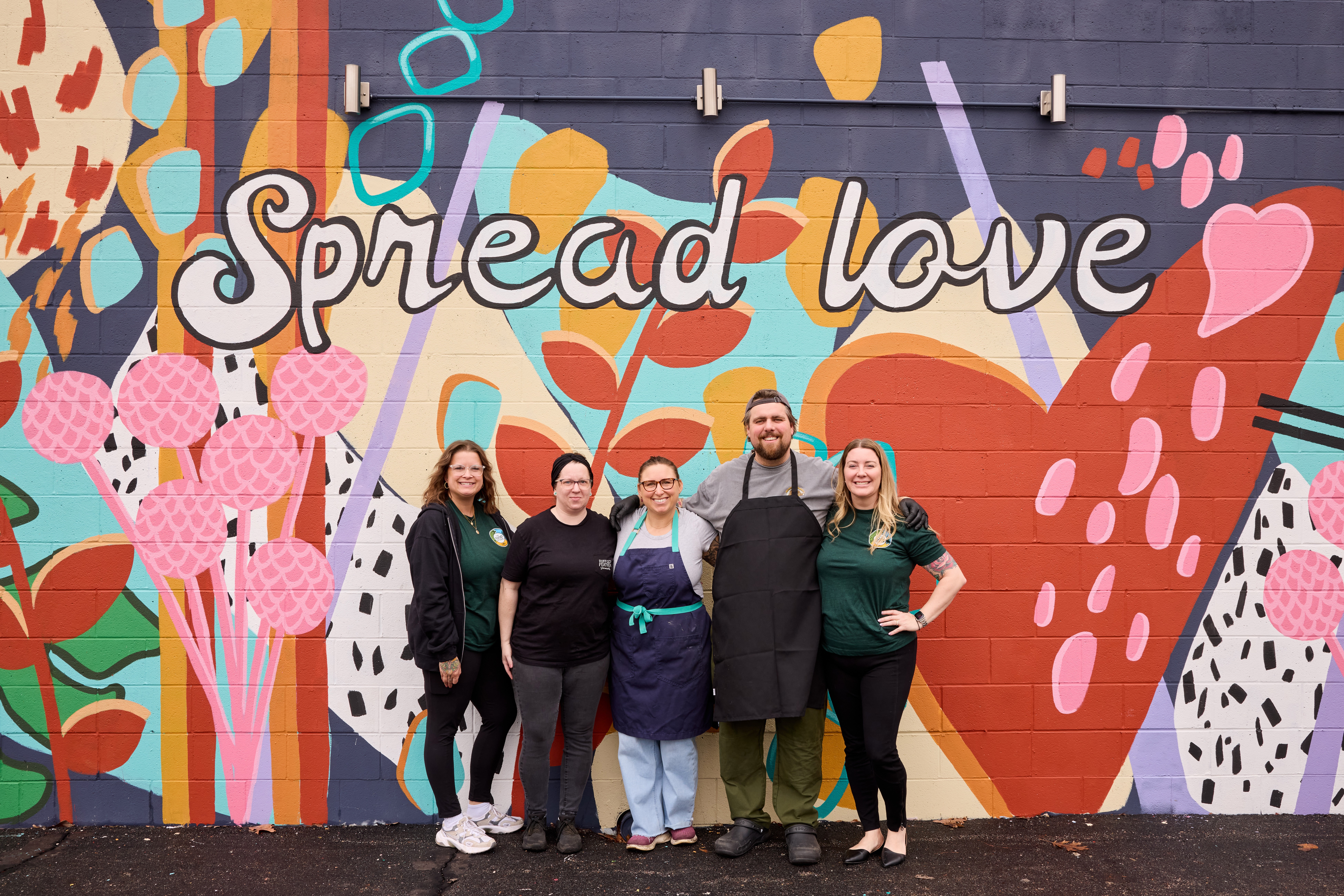 Group of five people standing in front of a colorful mural with the words 'Spread love' and various abstract shapes.