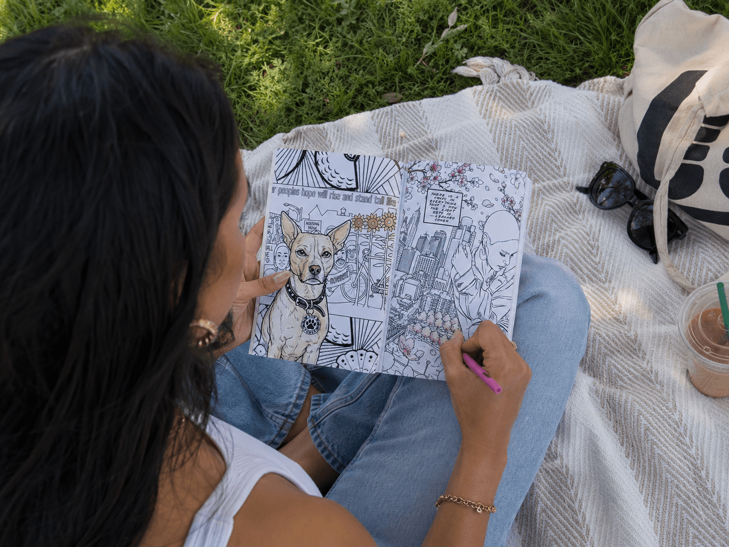Person sitting outdoors on a blanket, coloring a detailed drawing of a dog with a pink marker.