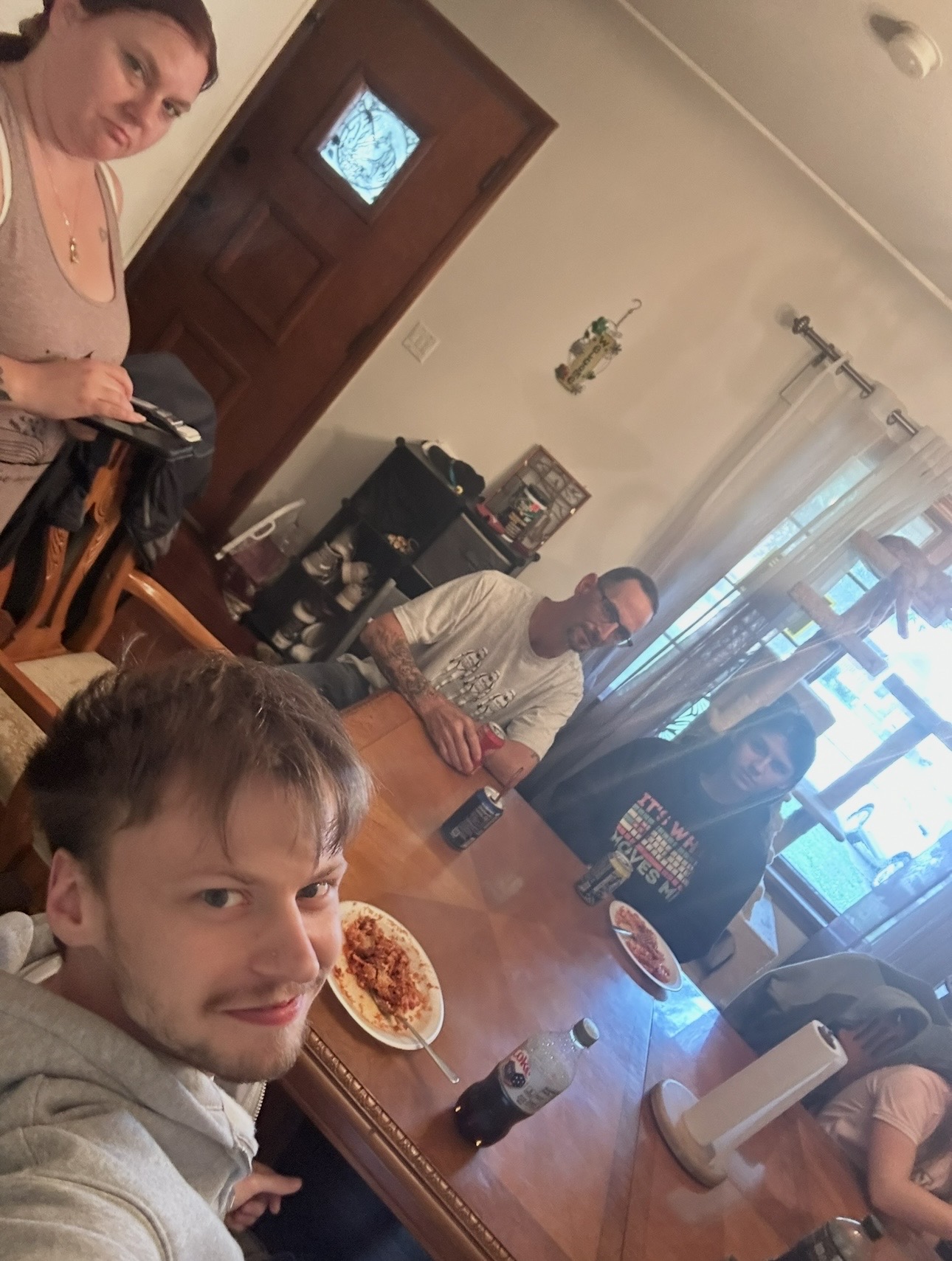 Four people sitting and standing around a dining table with food and drinks in a room with a door and window.