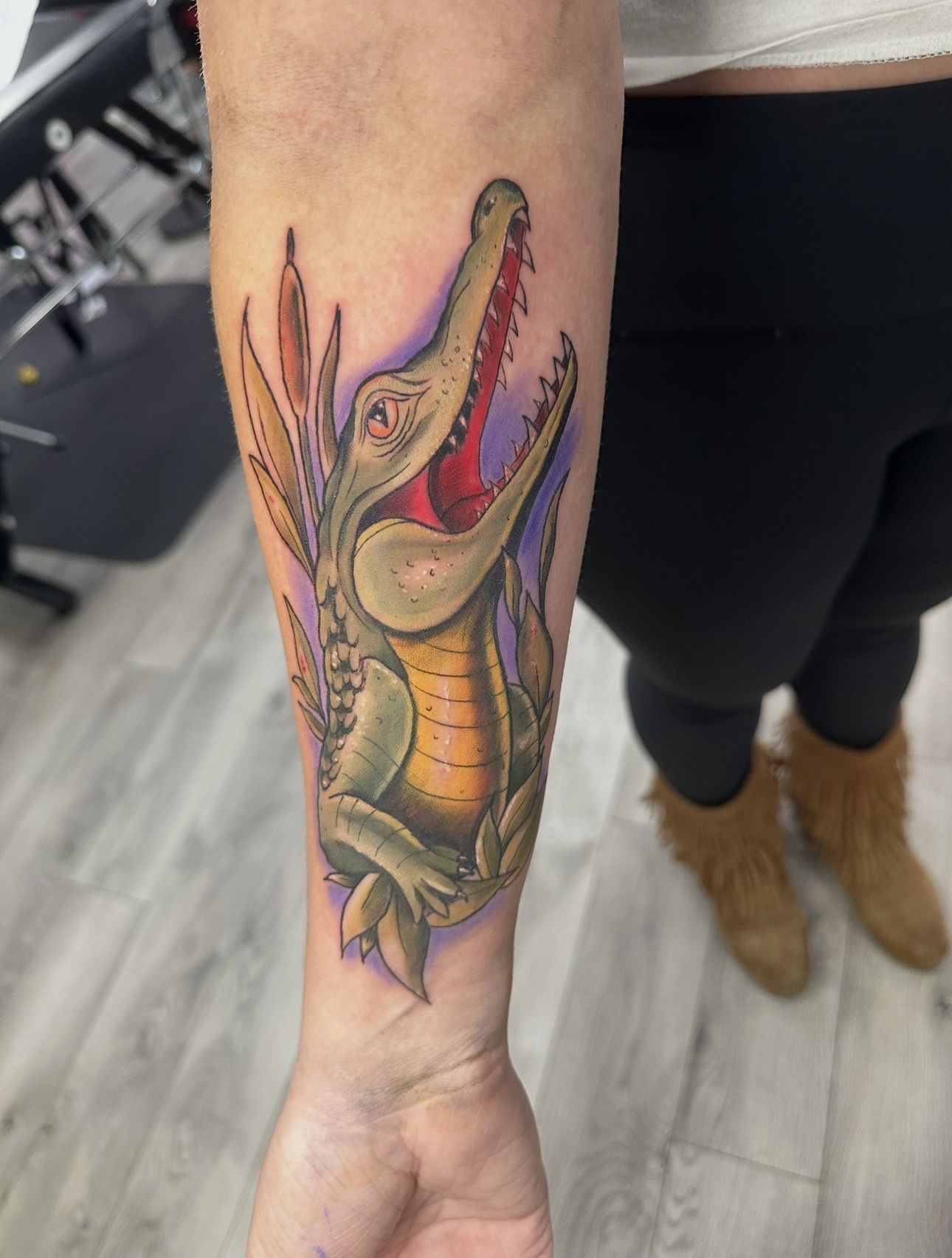 Colorful crocodile tattoo on person's forearm, with open mouth and detailed scales, in a realistic style.