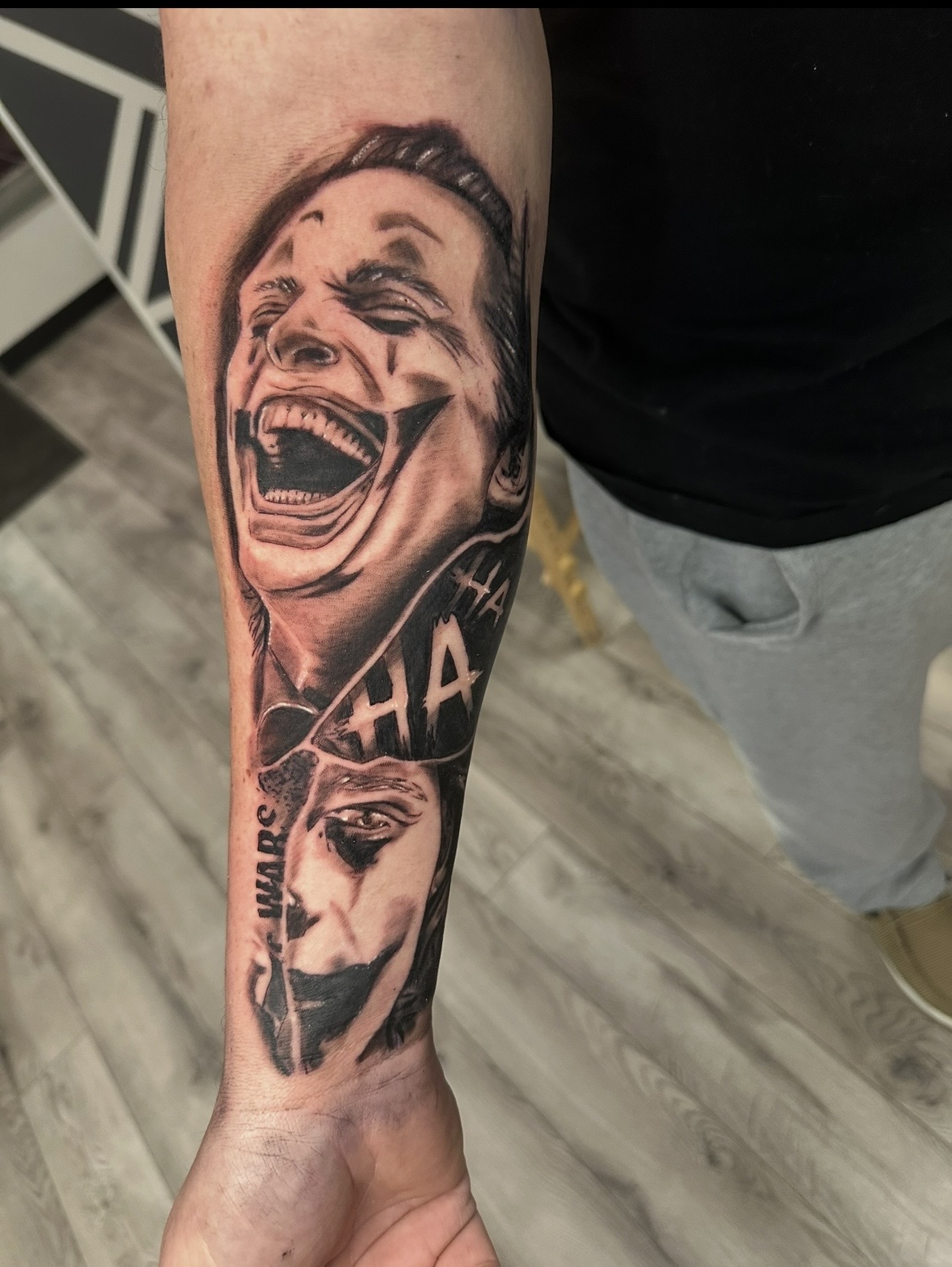 Tattoo of a laughing woman's face and a dog's face on person's arm, with text and shading details.