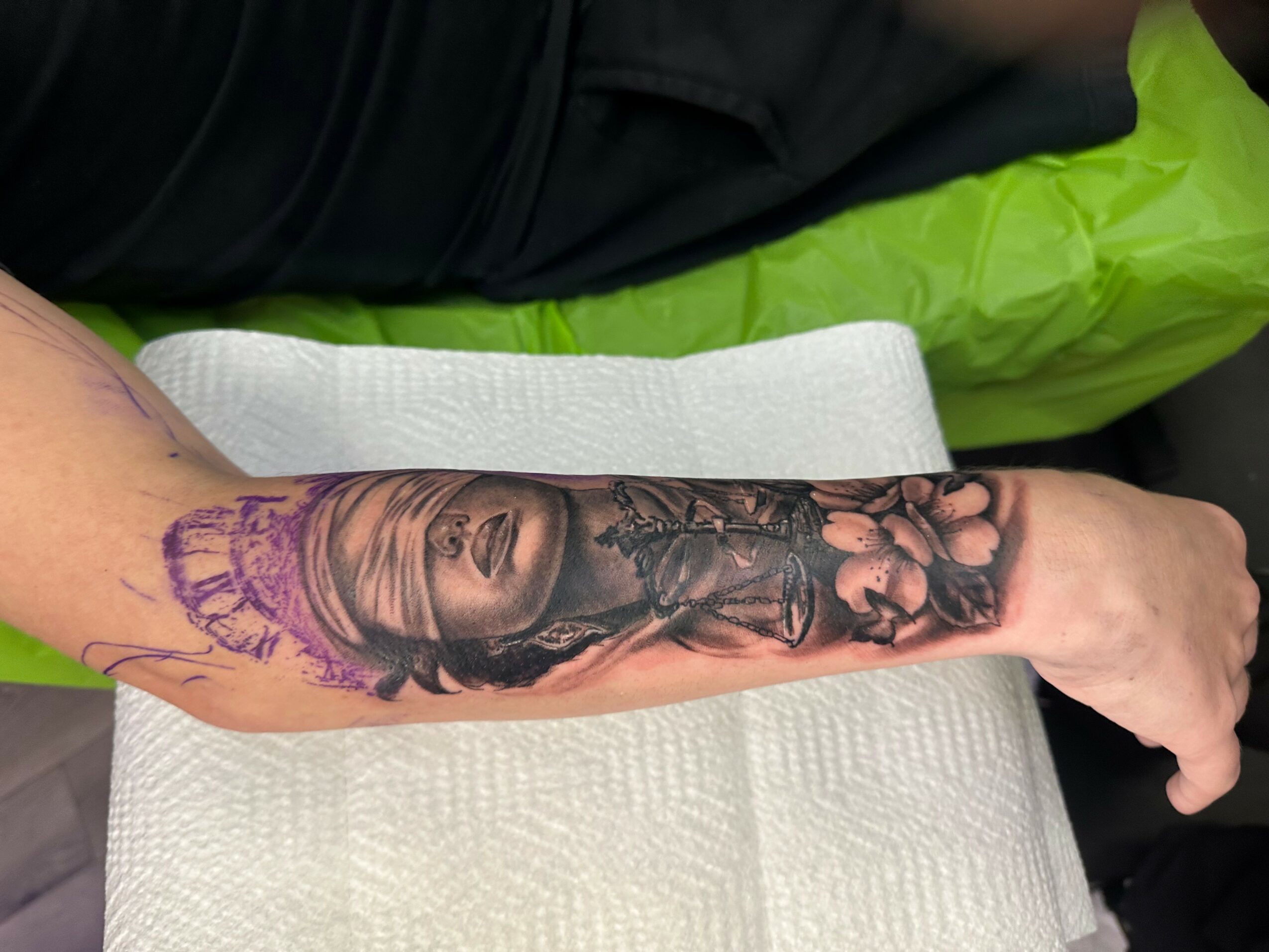 Tattoo of a woman's face and flowers on a person's forearm, with purple ink outlines, lying on a white towel.