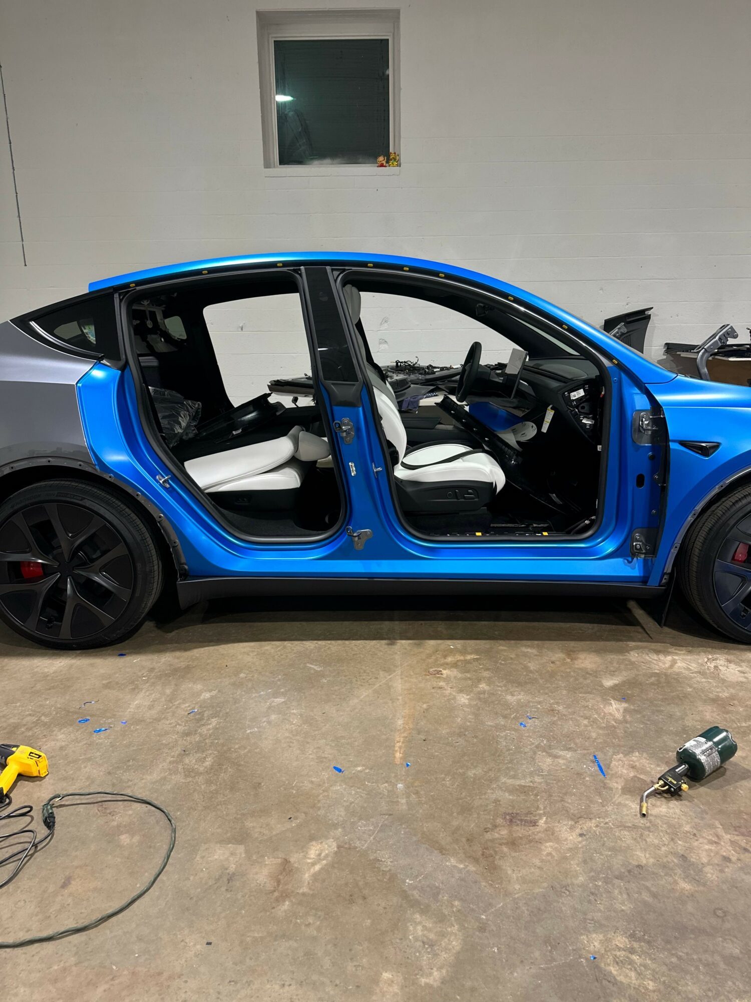 Blue compact car with open door, interior visible, parked indoors on concrete floor, with a small object nearby.