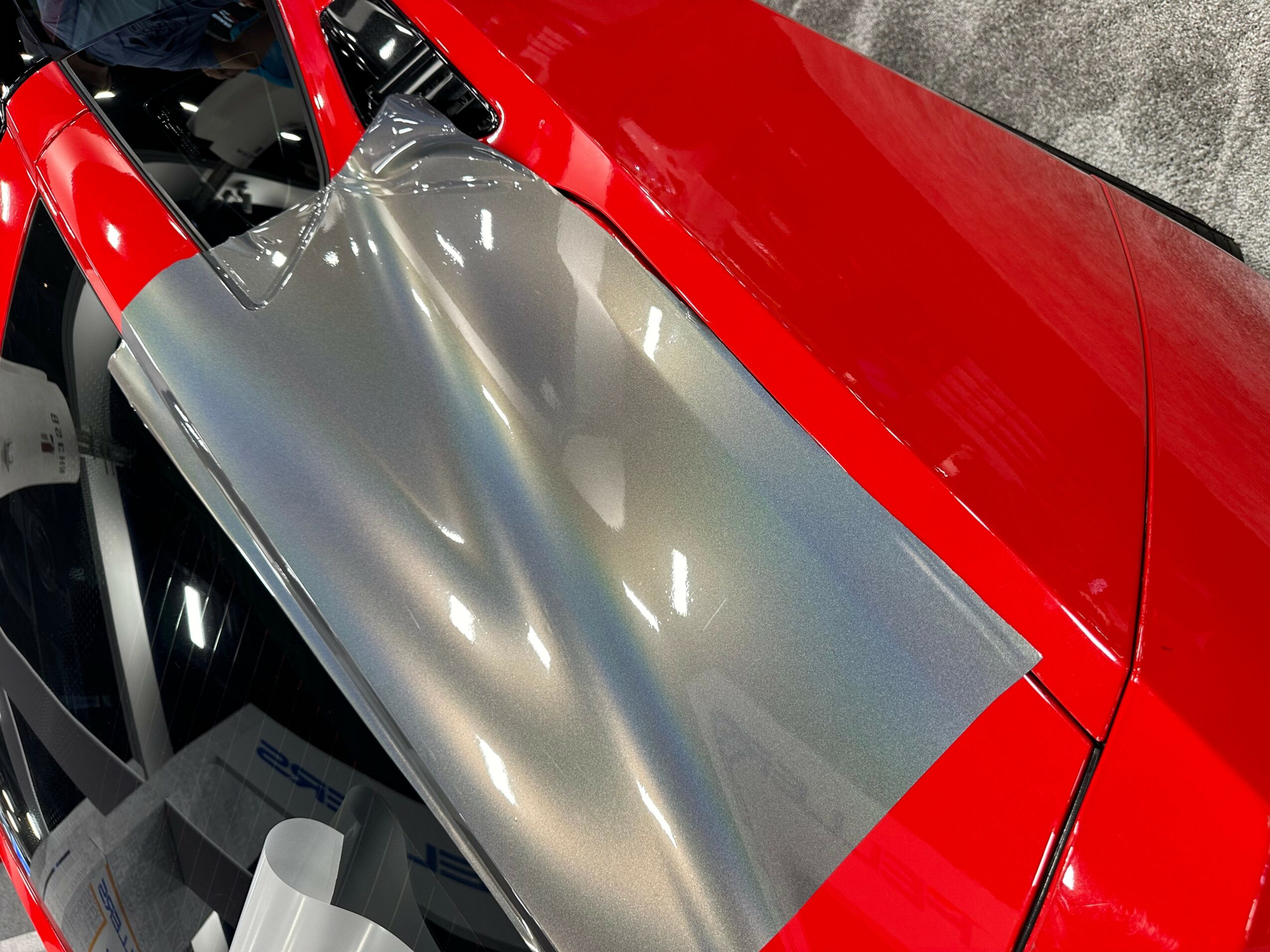 Red and silver car with reflective surface, showing part of the hood and side panel.