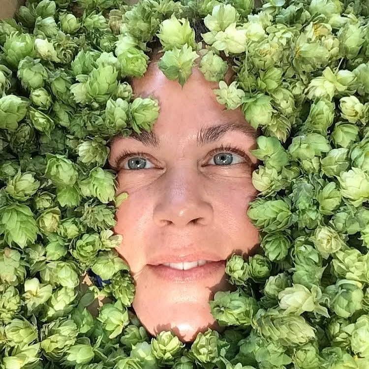 Person's face surrounded by green leaves and flowers, with visible blue eyes and a slight smile.