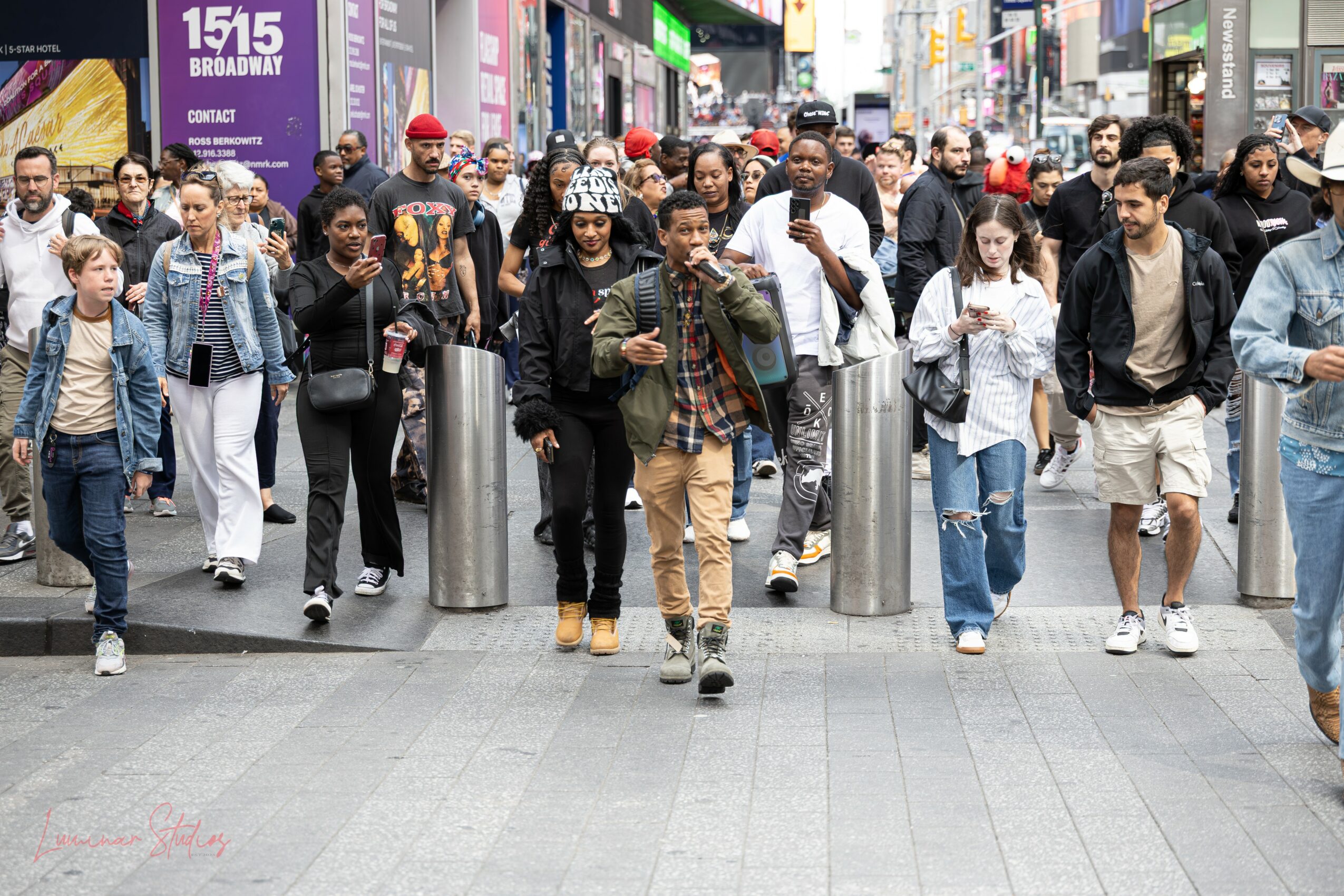 Crowd of diverse people walking on city street, some looking at phones, others talking, with storefronts and signs in background.