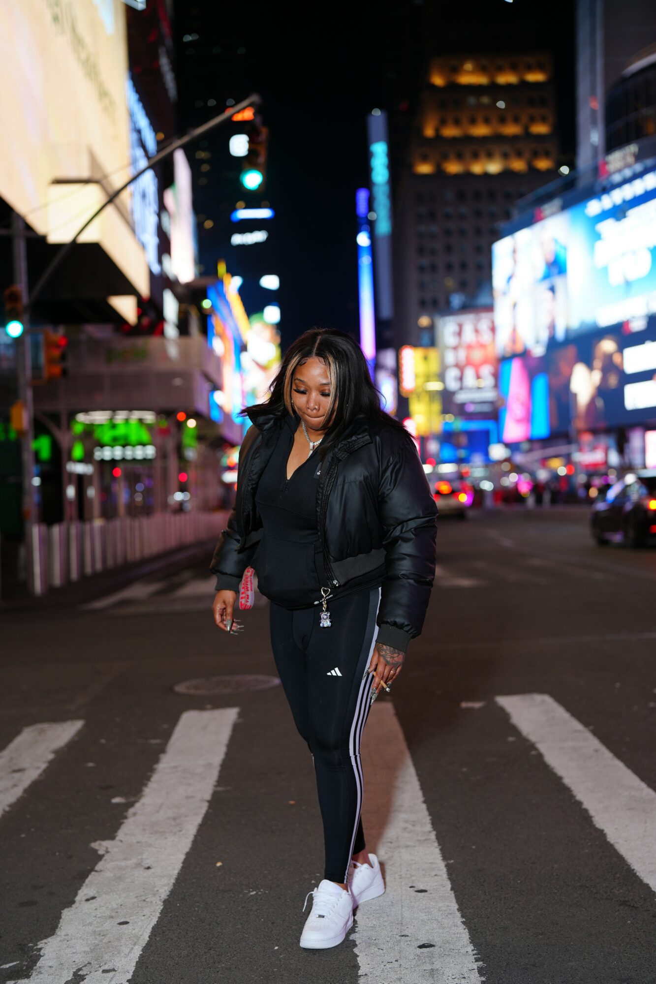 Woman walking across a city street at night with bright lights and billboards in the background.