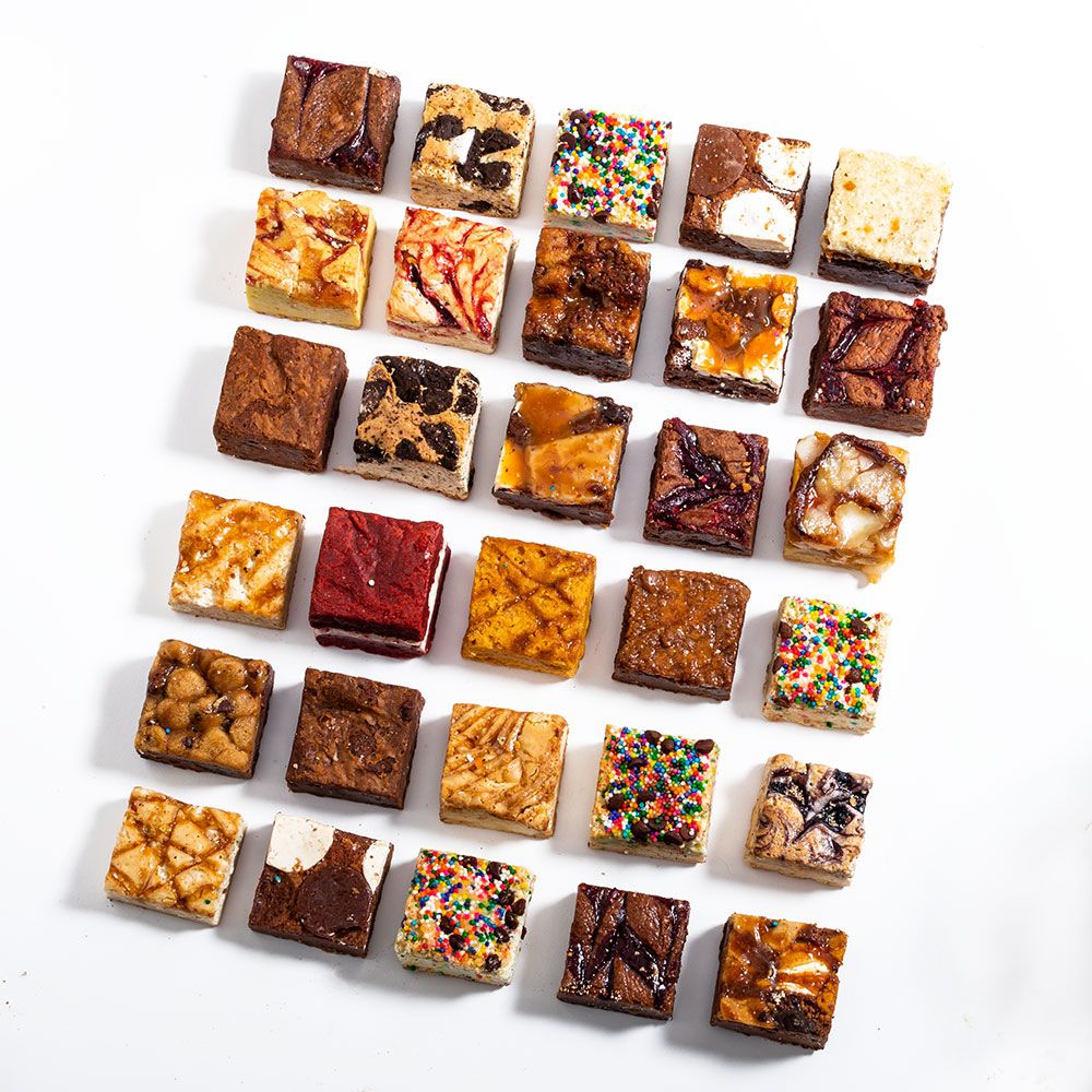 Assorted small dessert squares with various toppings and fillings arranged in rows on a white background.