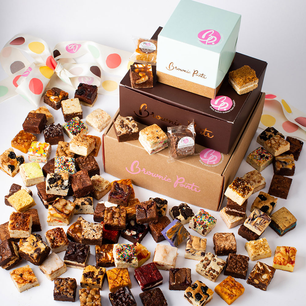 Assorted brownie bites and bars with colorful toppings and wrappers, scattered around boxes on a white surface.