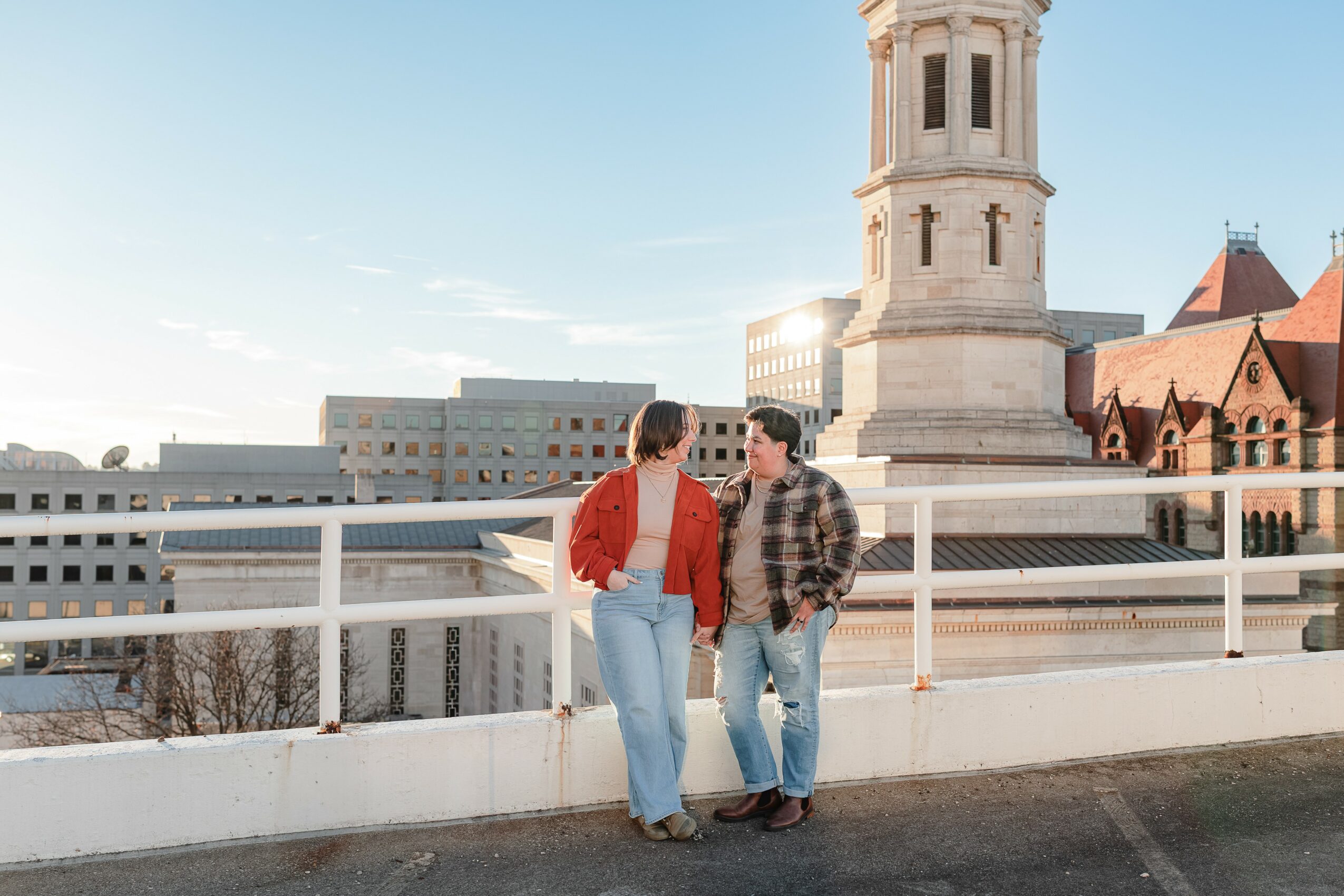 Two women stand on a rooftop with a cityscape and historic building in the background, talking and smiling.
