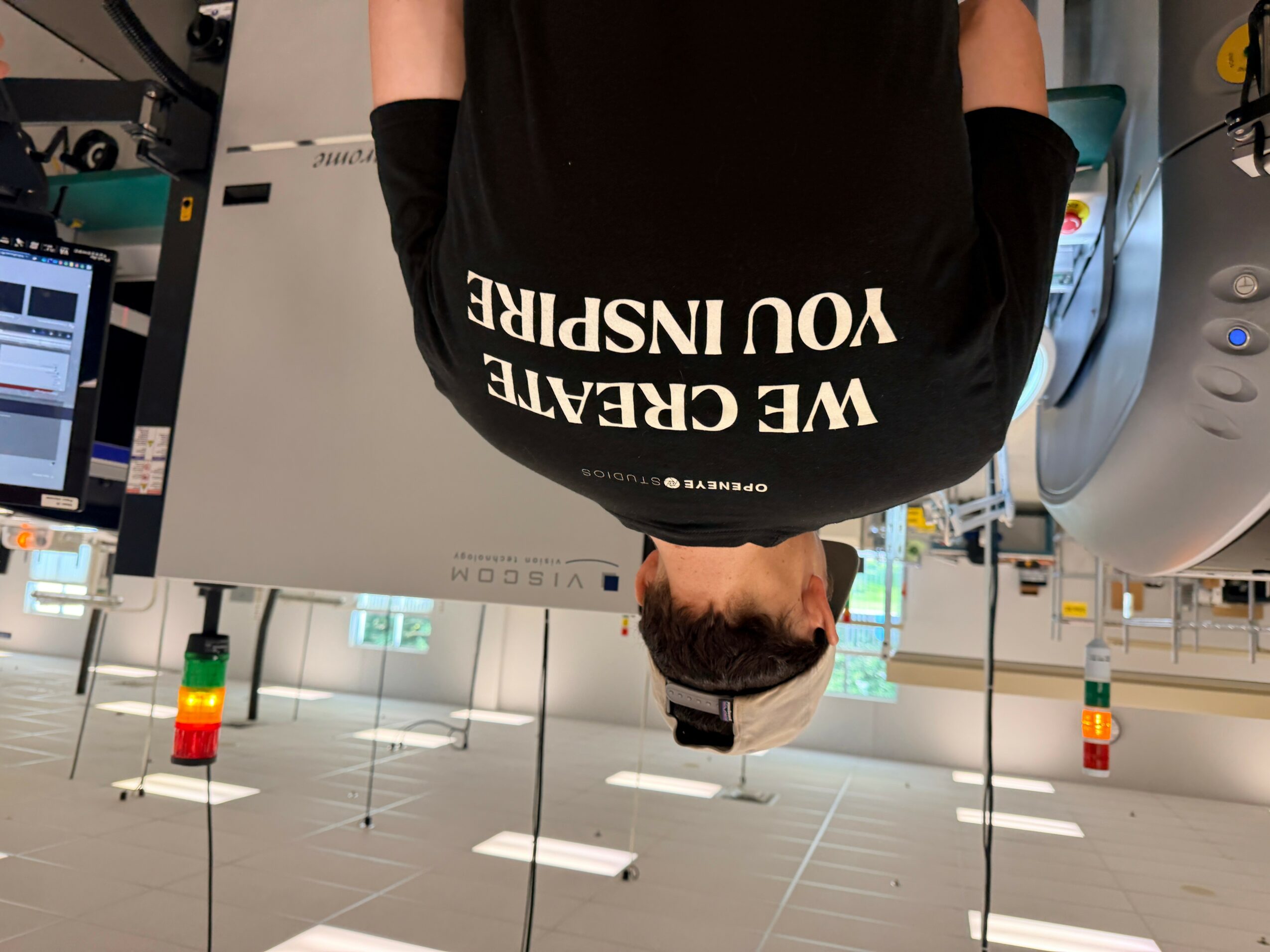 Person with dark hair and glasses in a black shirt with white text, standing in a modern indoor space.